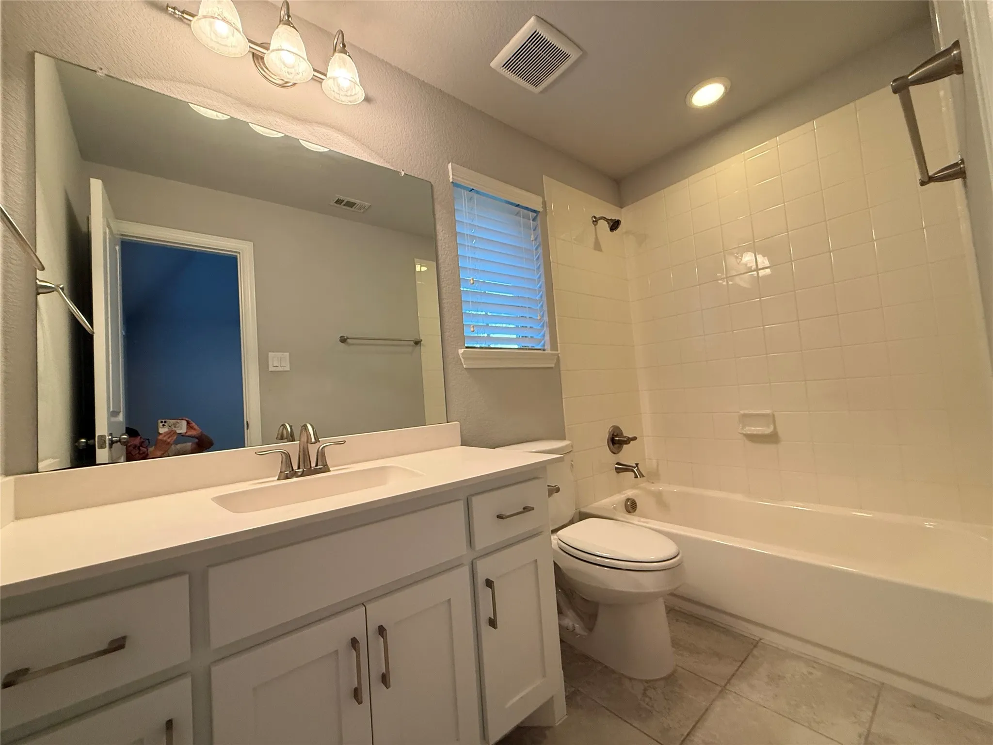 White vanity with an integrated sink, brushed nickel faucet, large mirror, and tiled flooring
