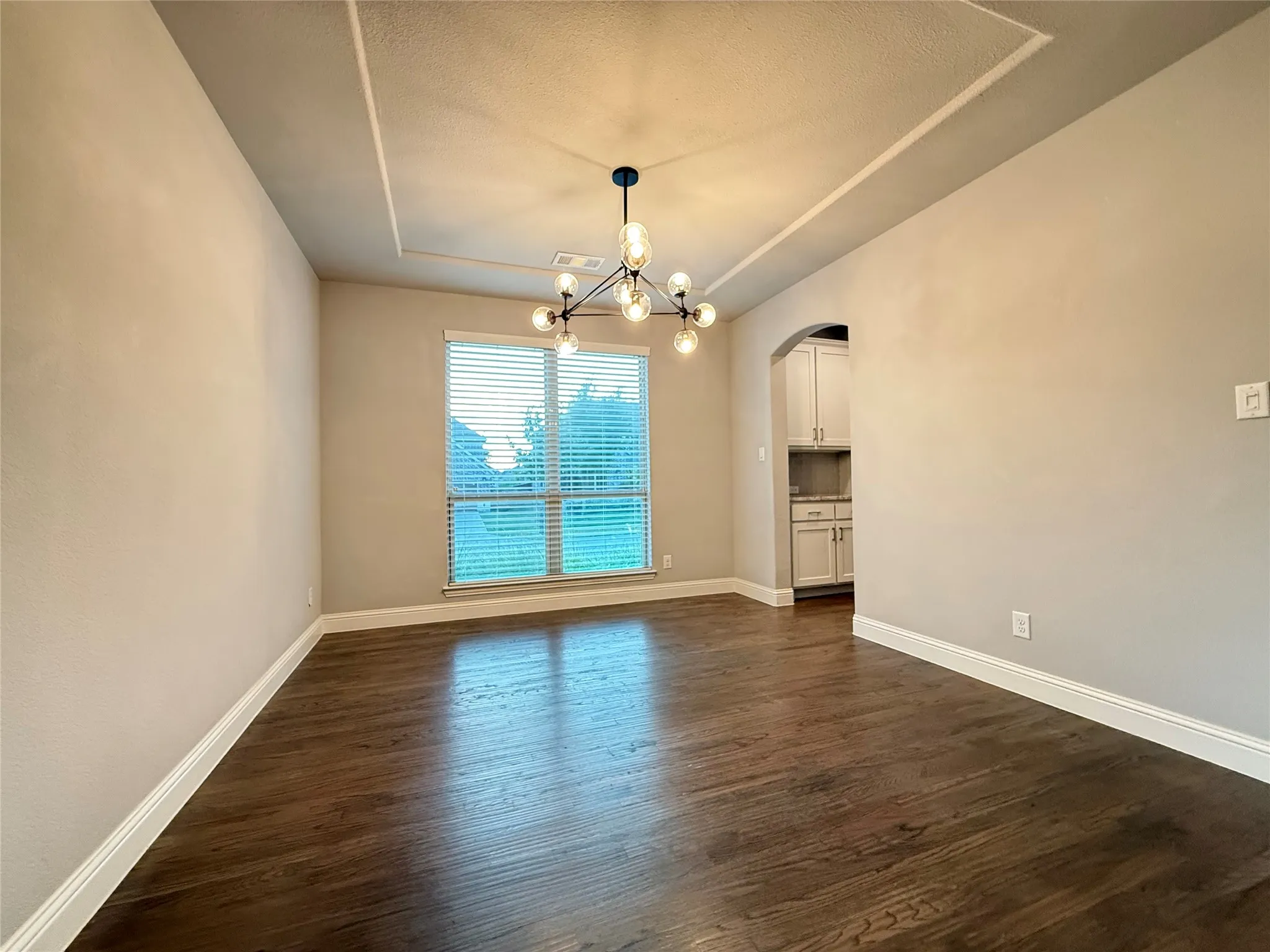 Tray ceiling with a contemporary chandelier, wood-finish flooring, and arched doorway