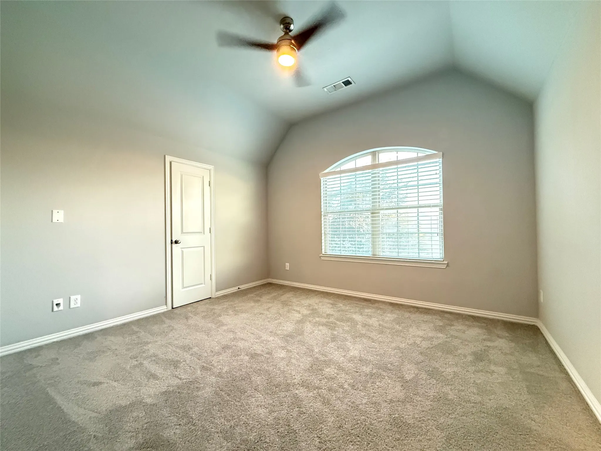 Vaulted ceiling with an arched window, ceiling fan, neutral wall paint, and light-colored carpet flooring