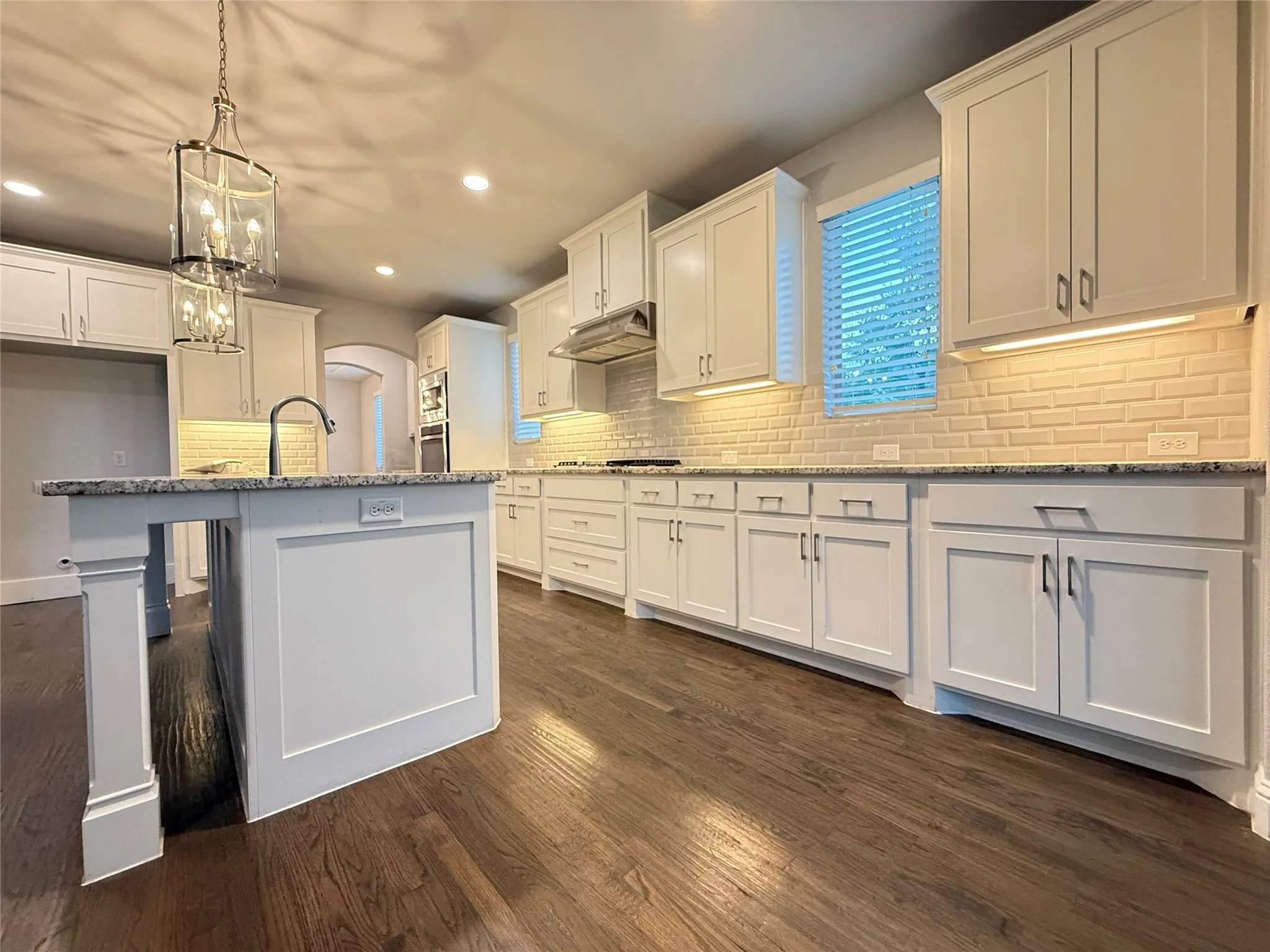 White shaker cabinetry, wood-finish flooring, undermount sink, subway tile backsplash, and an island with a stone countertop