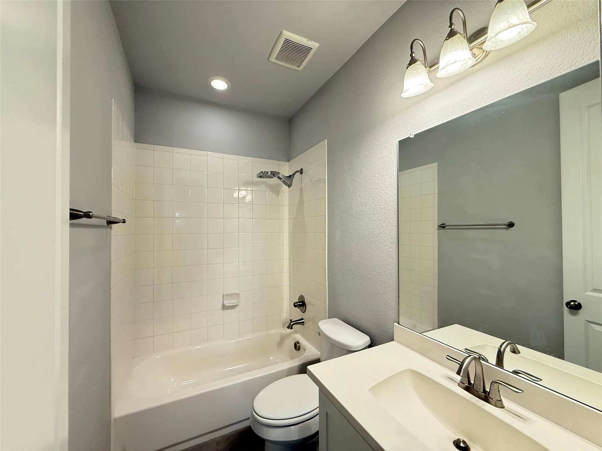 White tile bath surround, recessed ceiling lighting, vanity with integrated sink, brushed nickel faucet, and vanity mirror
