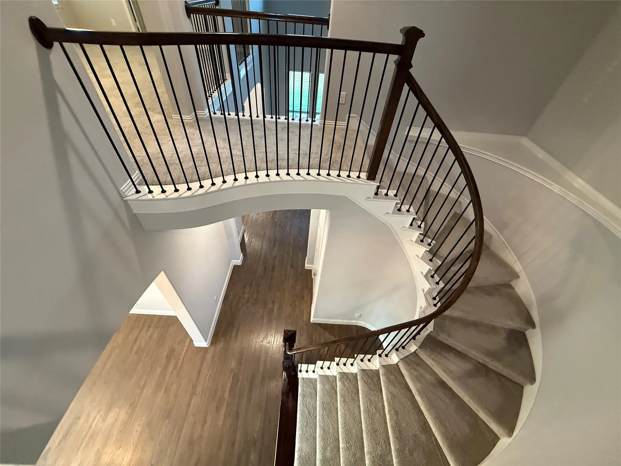 Curved staircase featuring dark wood handrails, black metal spindles, and light-toned carpeted treads
