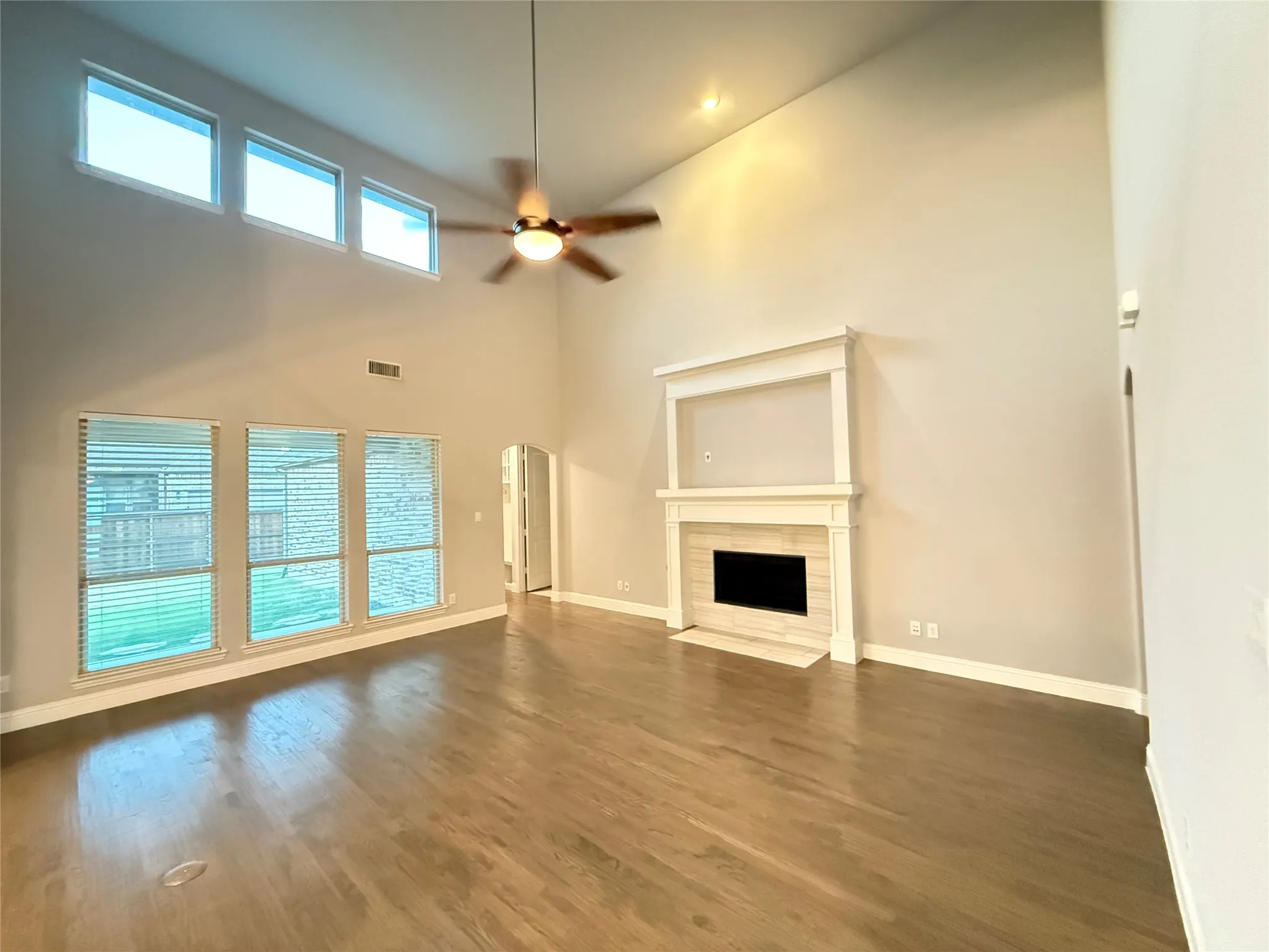 Vaulted ceiling, wood-finish flooring, built-in fireplace, ceiling fan with integrated lighting, and multiple windows