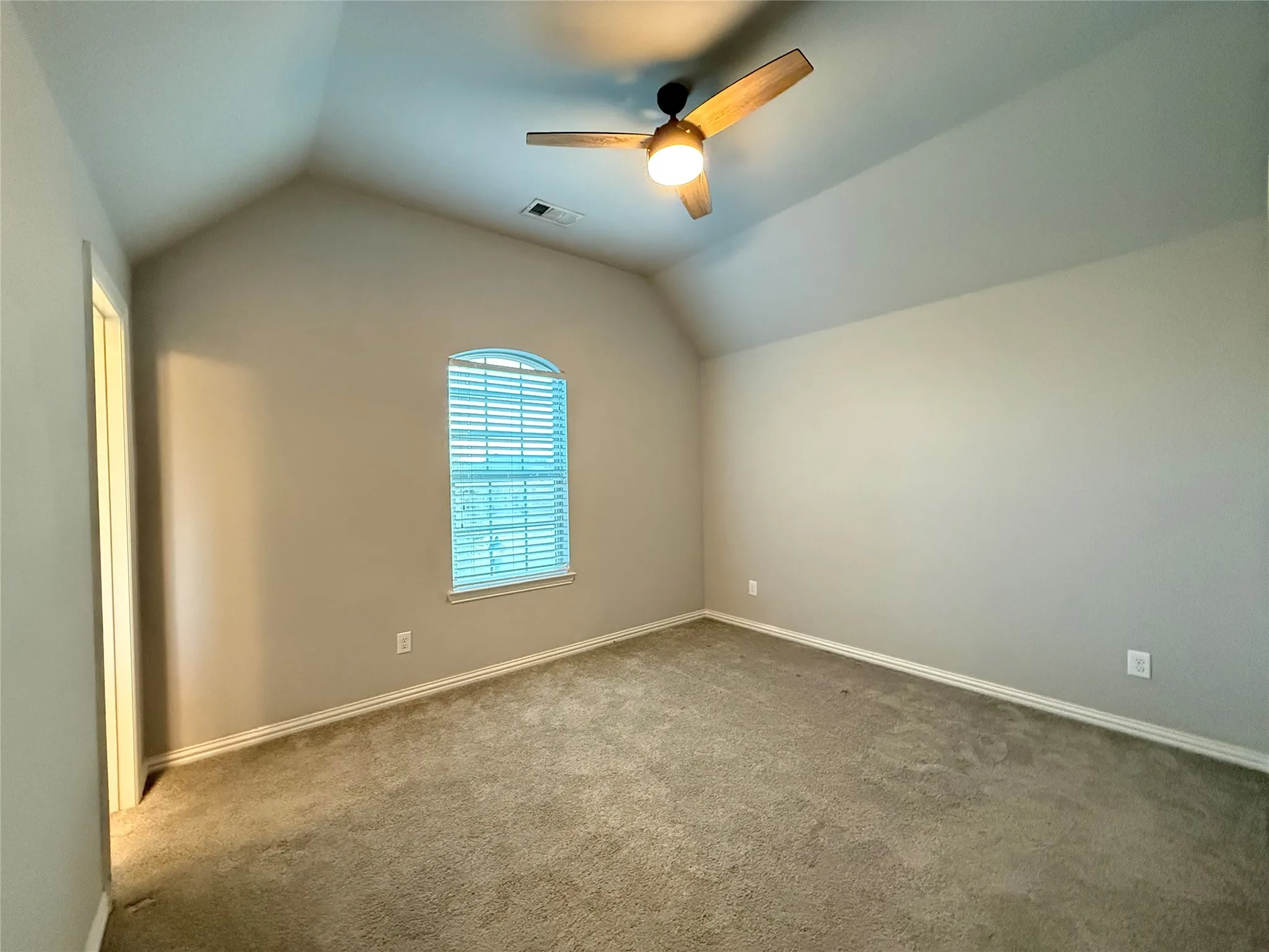 Vaulted ceiling with an attached ceiling fan, arched window with horizontal blinds, and neutral-toned carpeting
