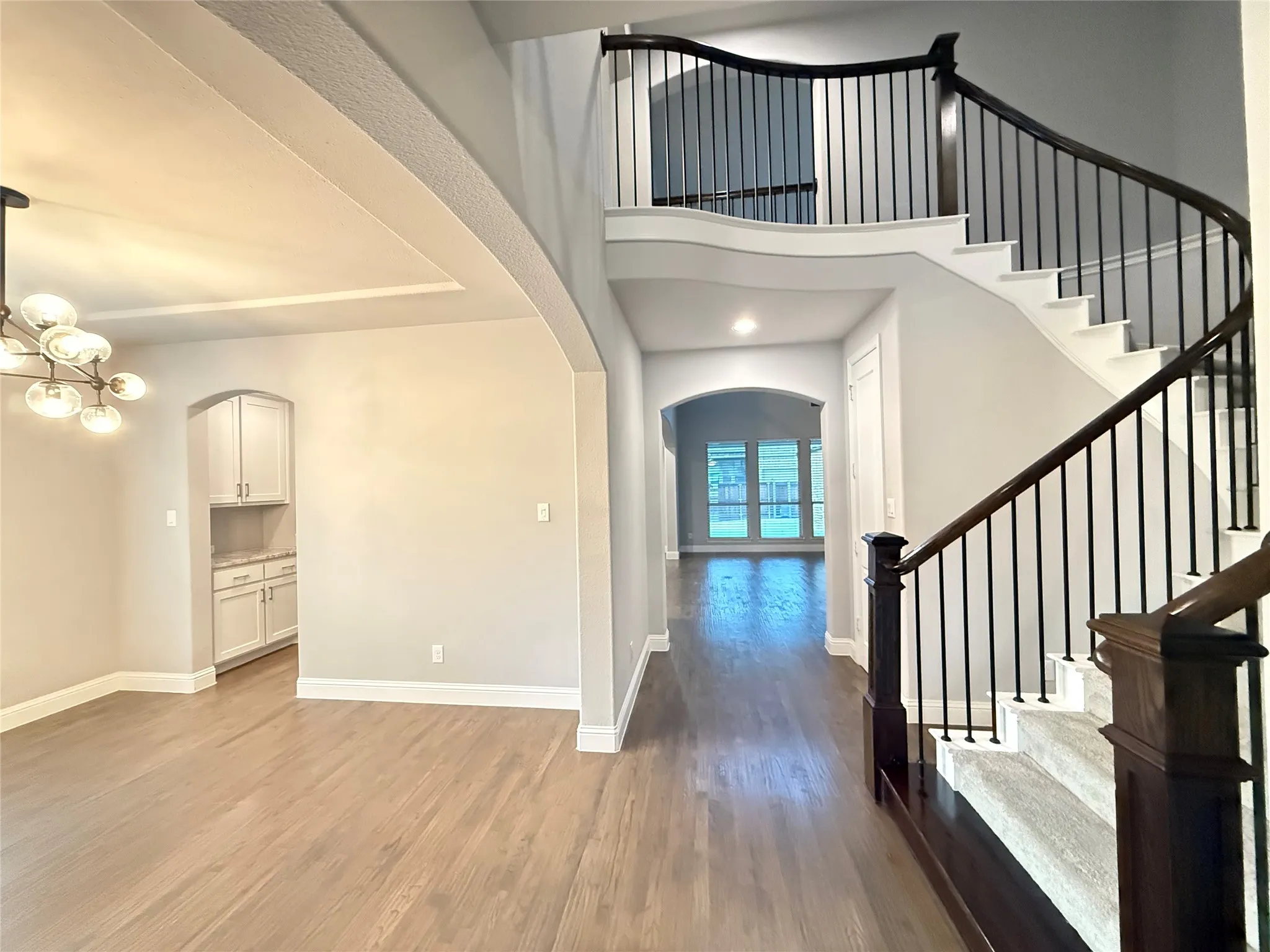Curved staircase with dark wood handrails and black metal balusters, tray ceiling with recessed lighting, wood-finish flooring, and arched doorways
