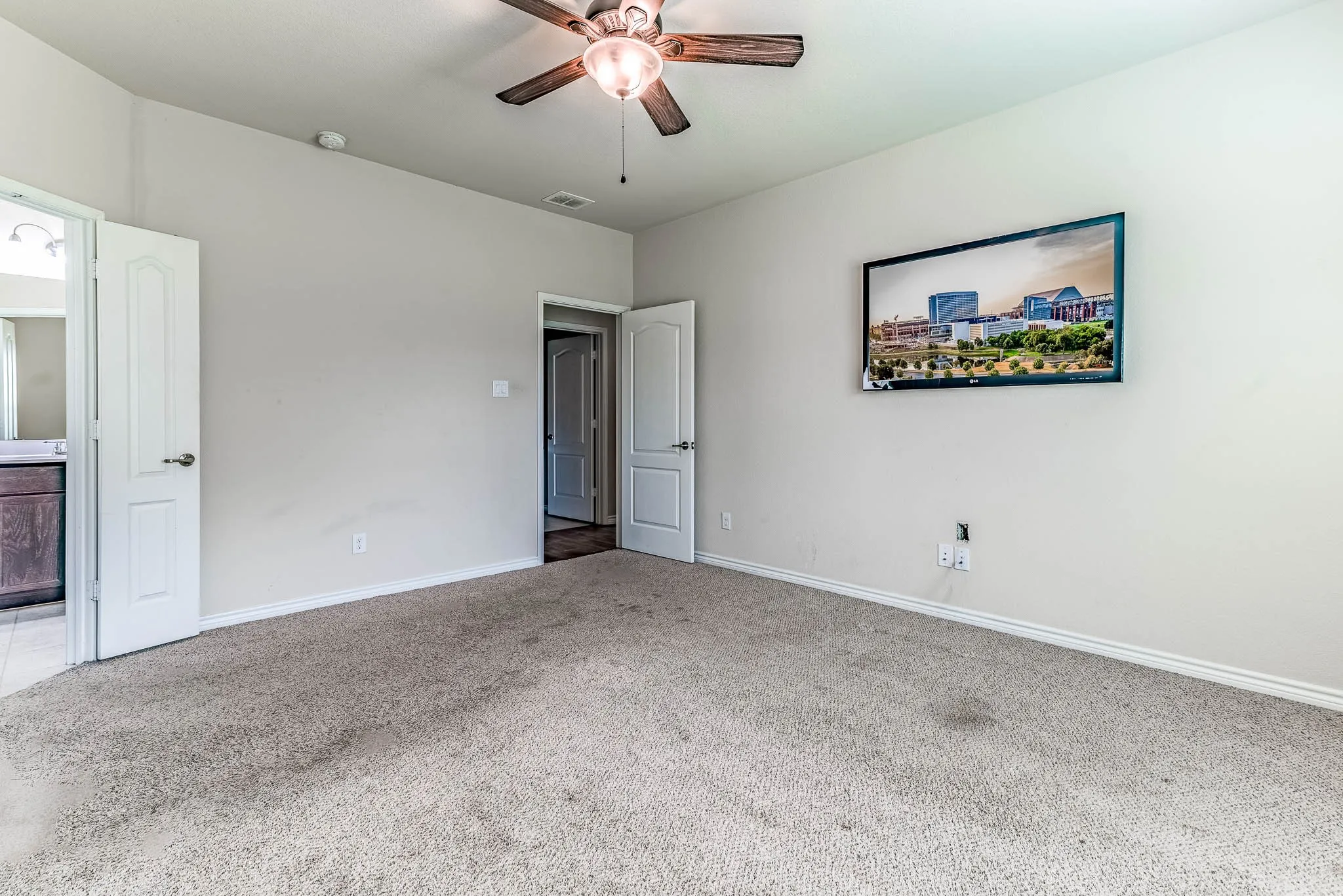 Primary bedroom with connected bathroom, carpet, ceiling fan