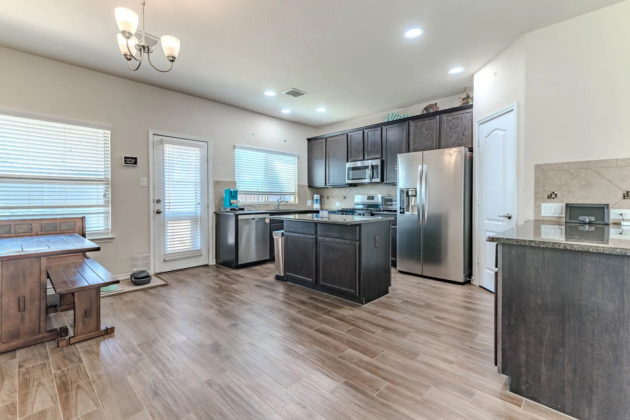 Kitchen with dark brown cabinets, tasteful back splash, sink, exhaust hood, and appliances with stainless steel finishes