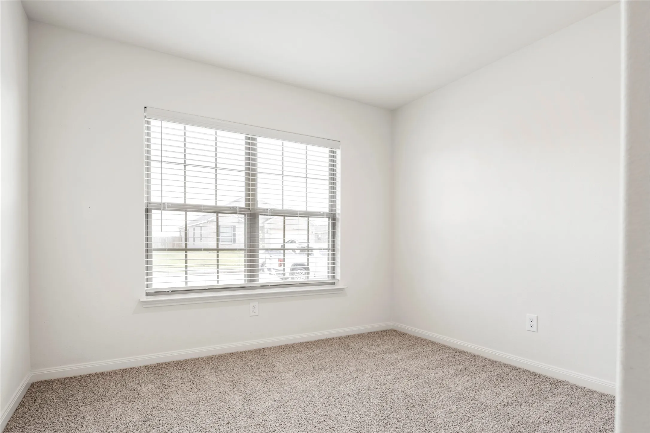 Front secondary bedroom. Neutral wall color, window with horizontal blinds, and carpeted flooring