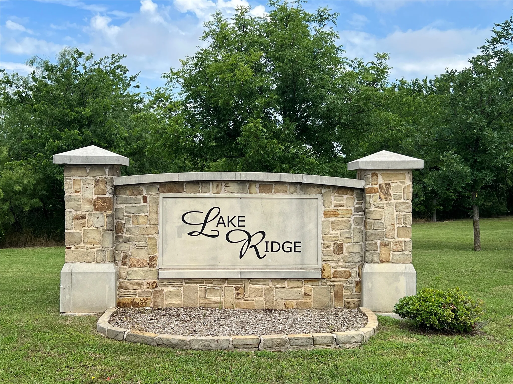 Stone entry monument with concrete capstones, integrated signage, and surrounding landscaping
