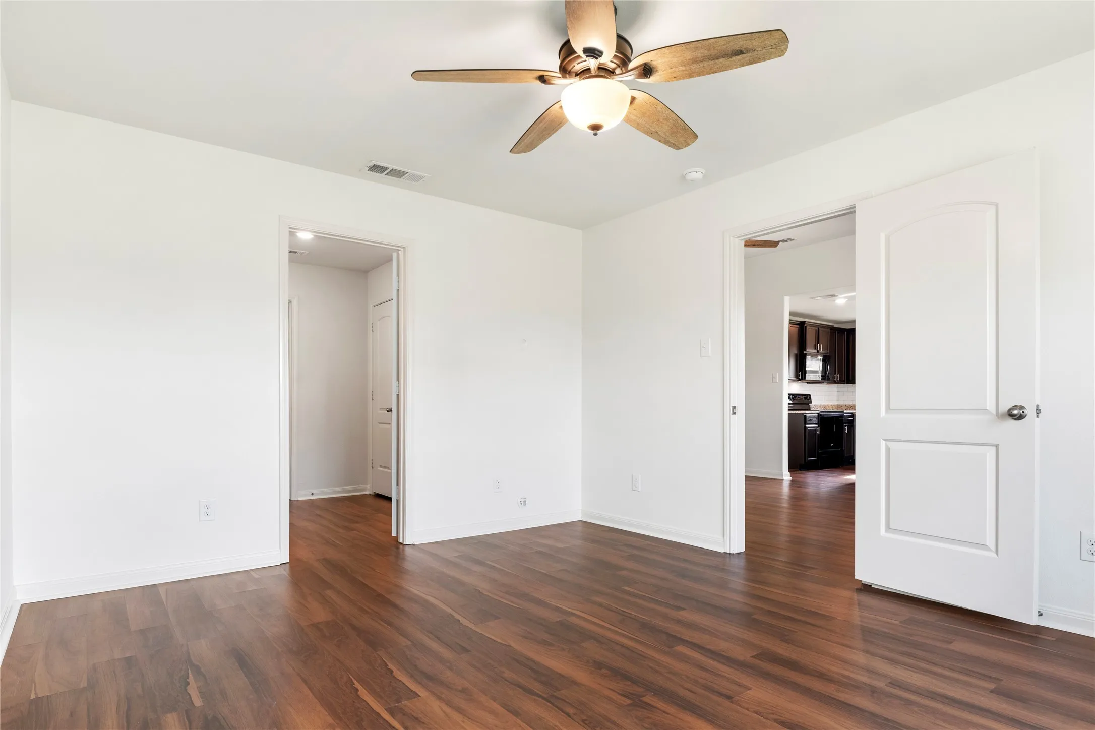 Second angled view of the Primary bedroom. Wood-finish LVP  flooring with white walls and a ceiling fan.
