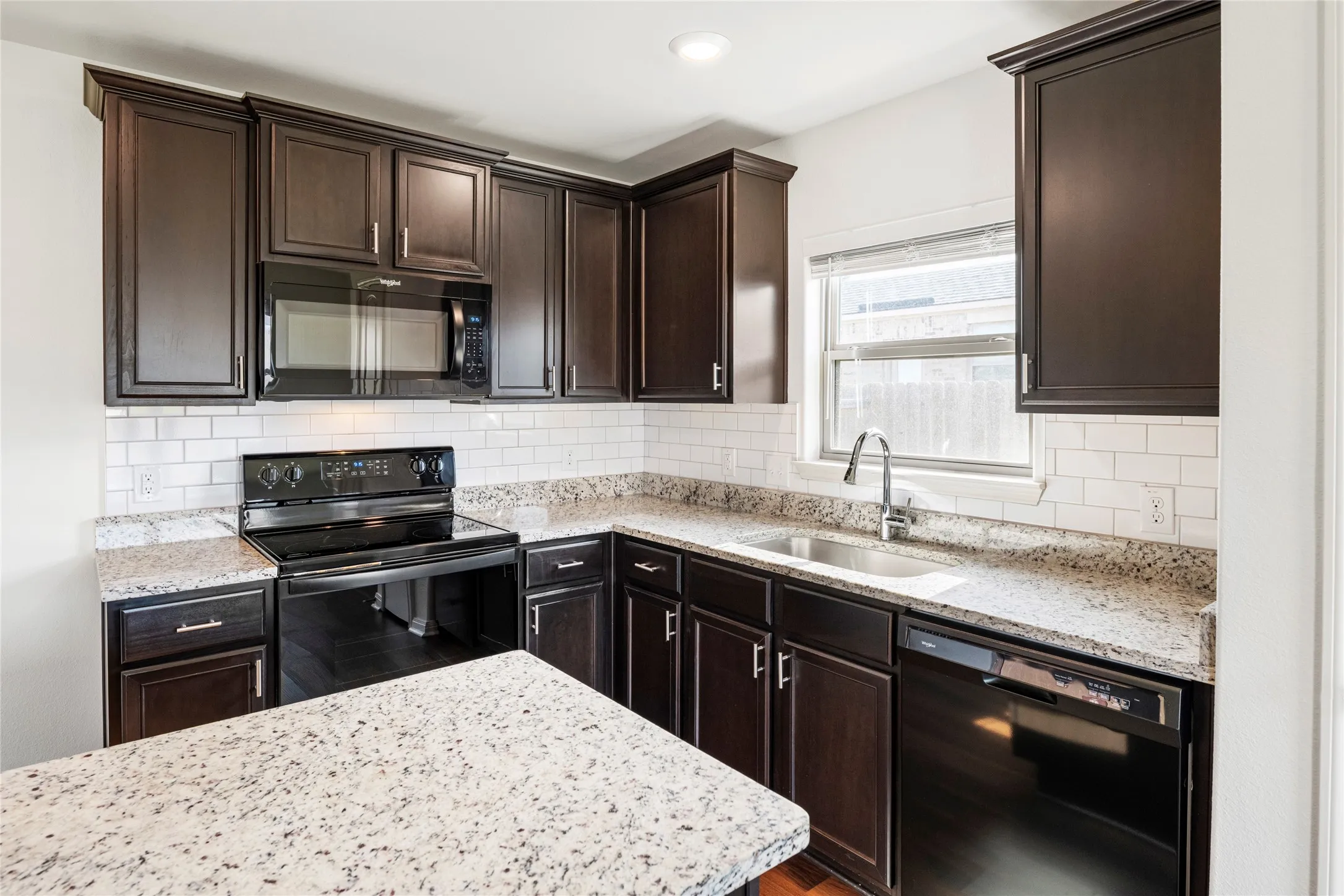 Kitchen featuring dark wood-finish cabinetry, granite countertops, subway tile backsplash, and black appliances