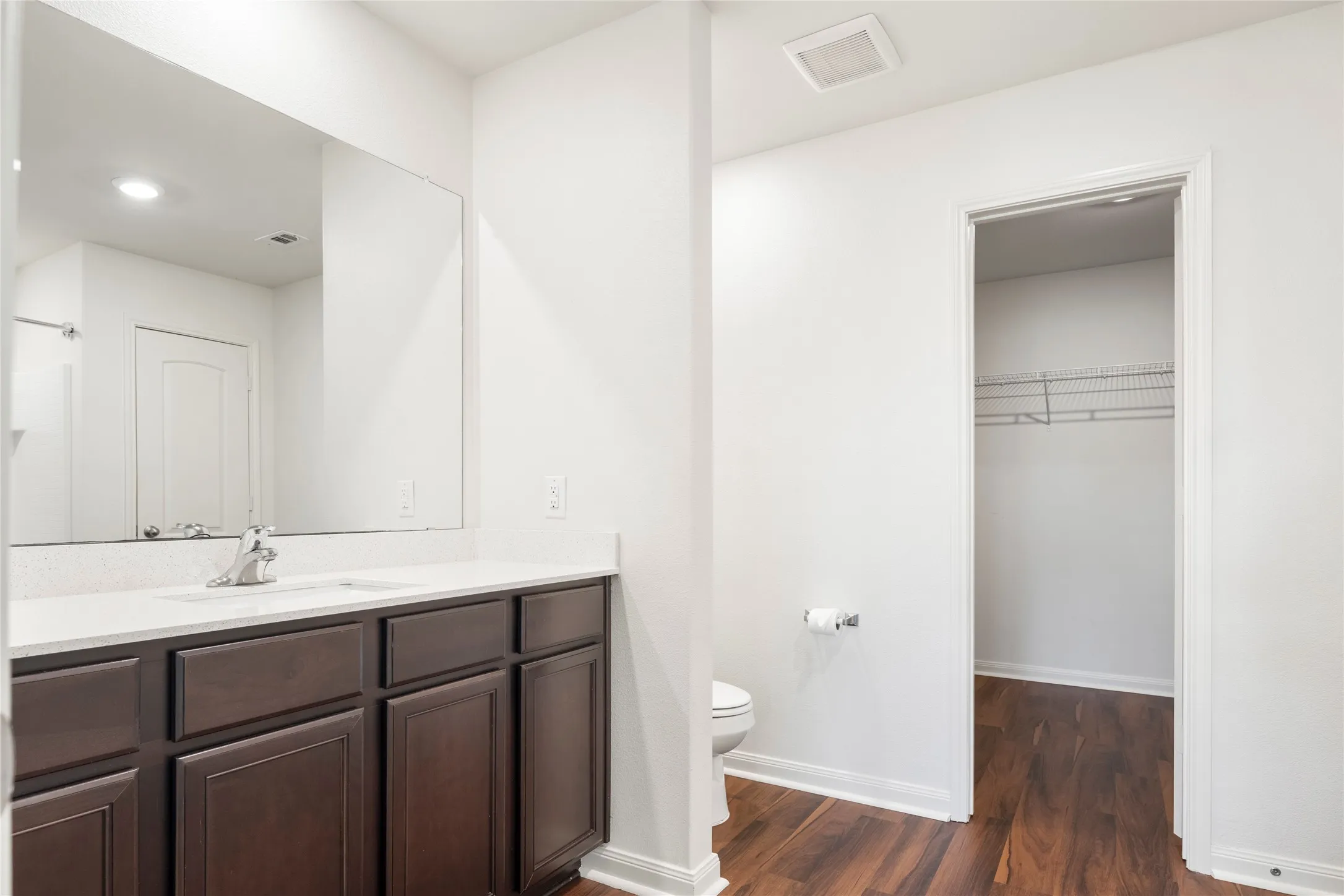 Bathroom featuring a dark wood-finish vanity with an integrated sink, polished chrome faucet, and expansive wall mirror