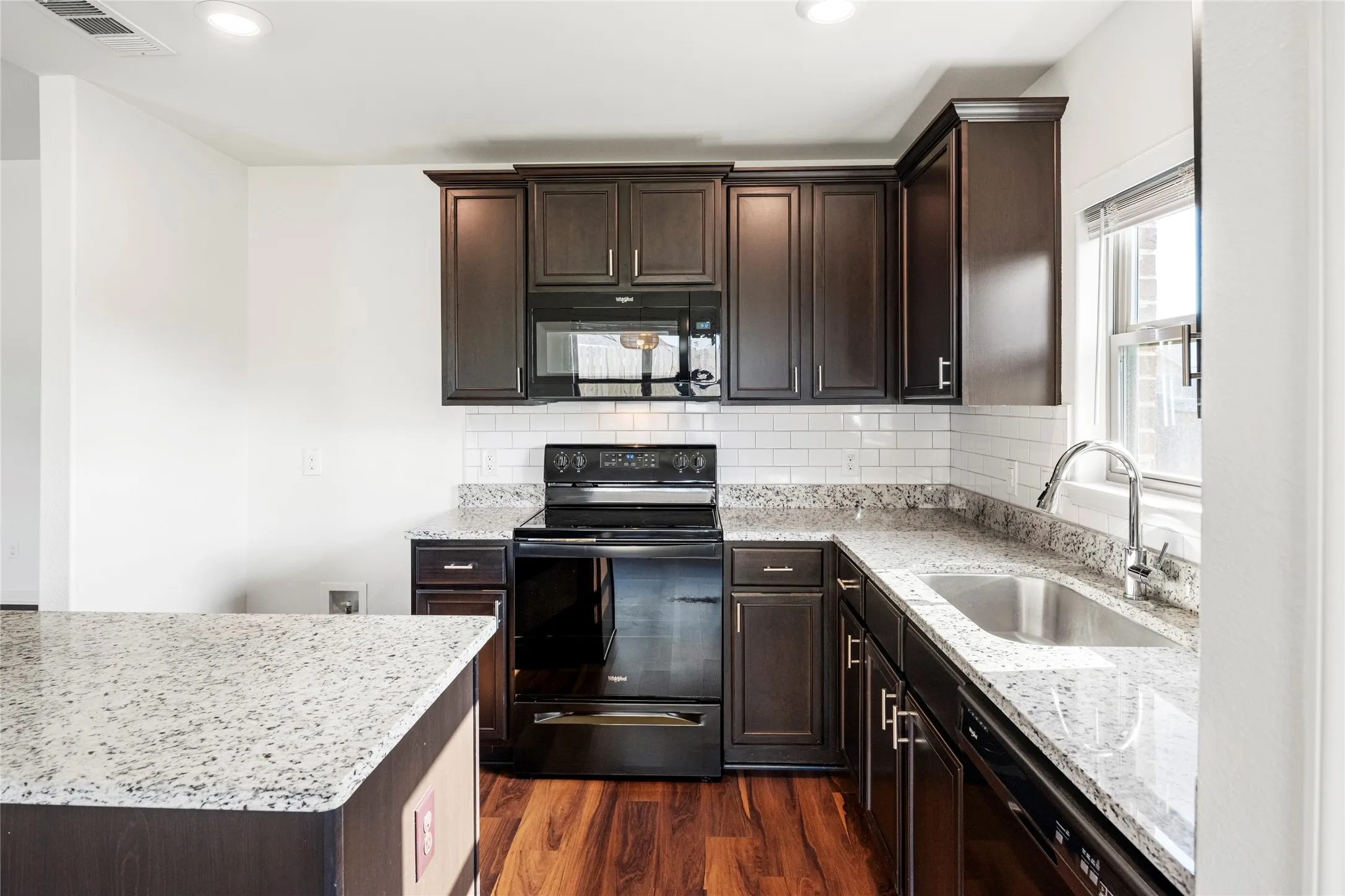 Kitchen featuring dark wood cabinetry, light speckled countertops, stainless steel sink with gooseneck faucet, black appliance suite, and wood-finish LVP  flooring