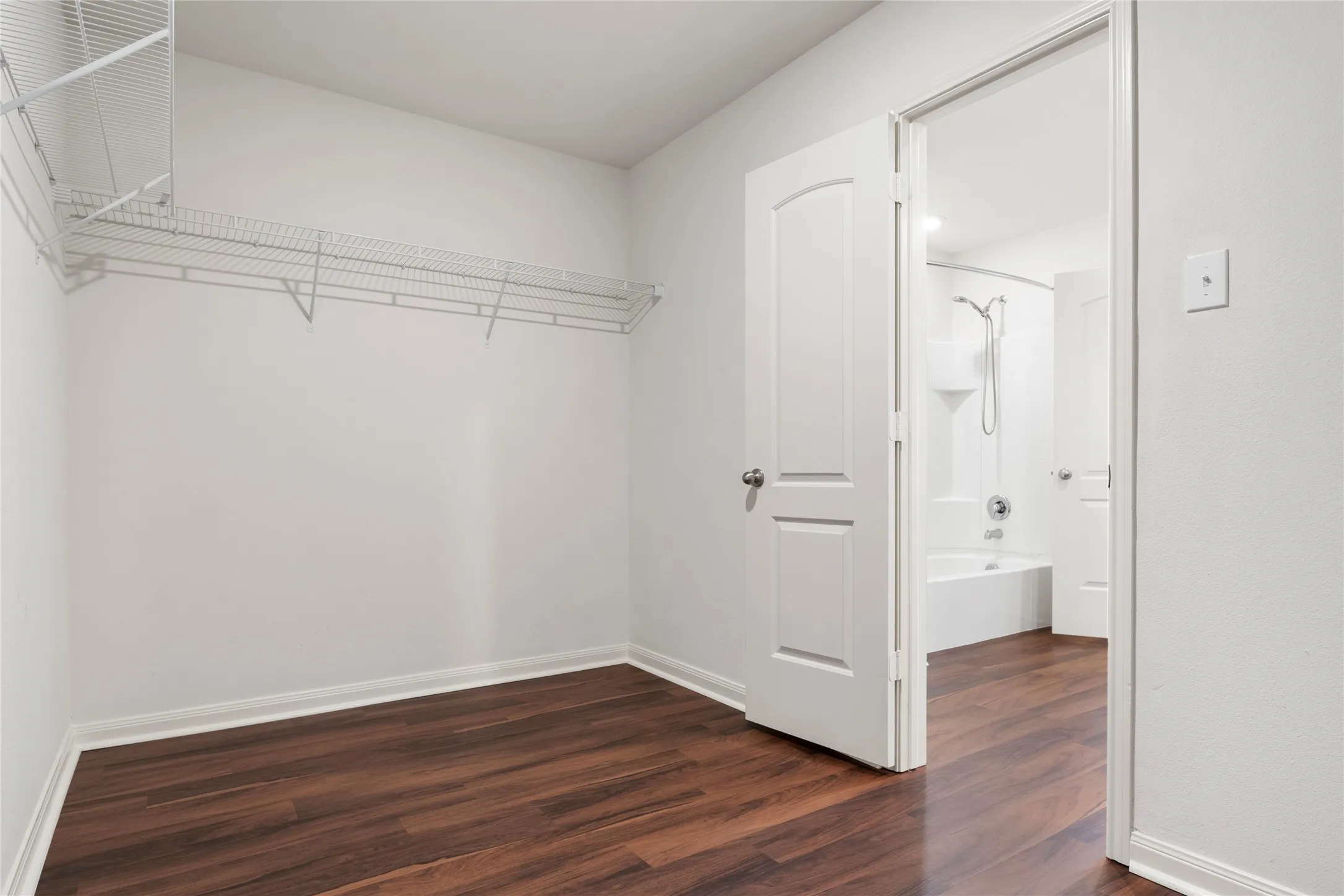 Primary Bedroom's walk in closet. Room features wood-finish LVP  flooring, white walls, and a wire shelving system.