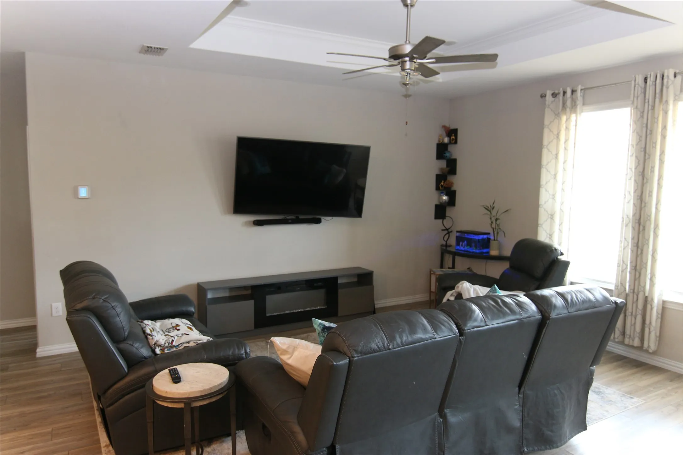 Tray ceiling with crown molding, ceiling fan, wood-finish flooring, and recessed electric fireplace