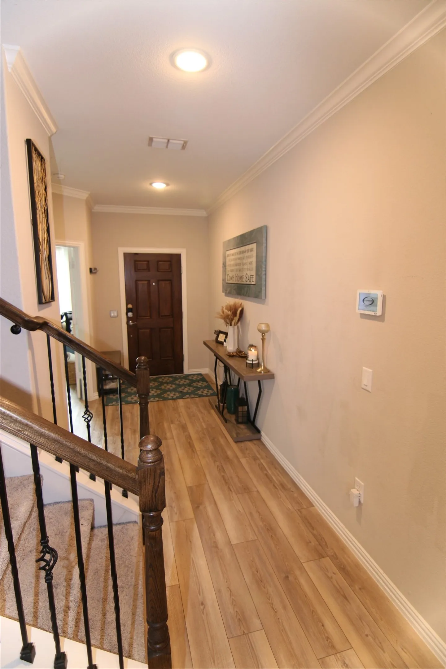 Wood-finish flooring, recessed lighting, crown molding, dark wood entry door, and a wrought iron and wood staircase railing