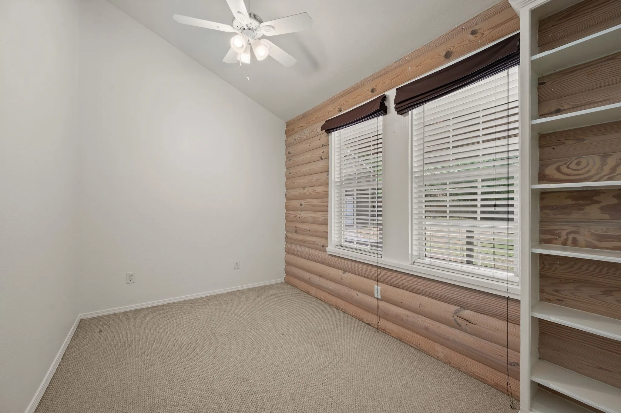 Carpeted empty room with ceiling fan, baseboards, log walls, and lofted ceiling