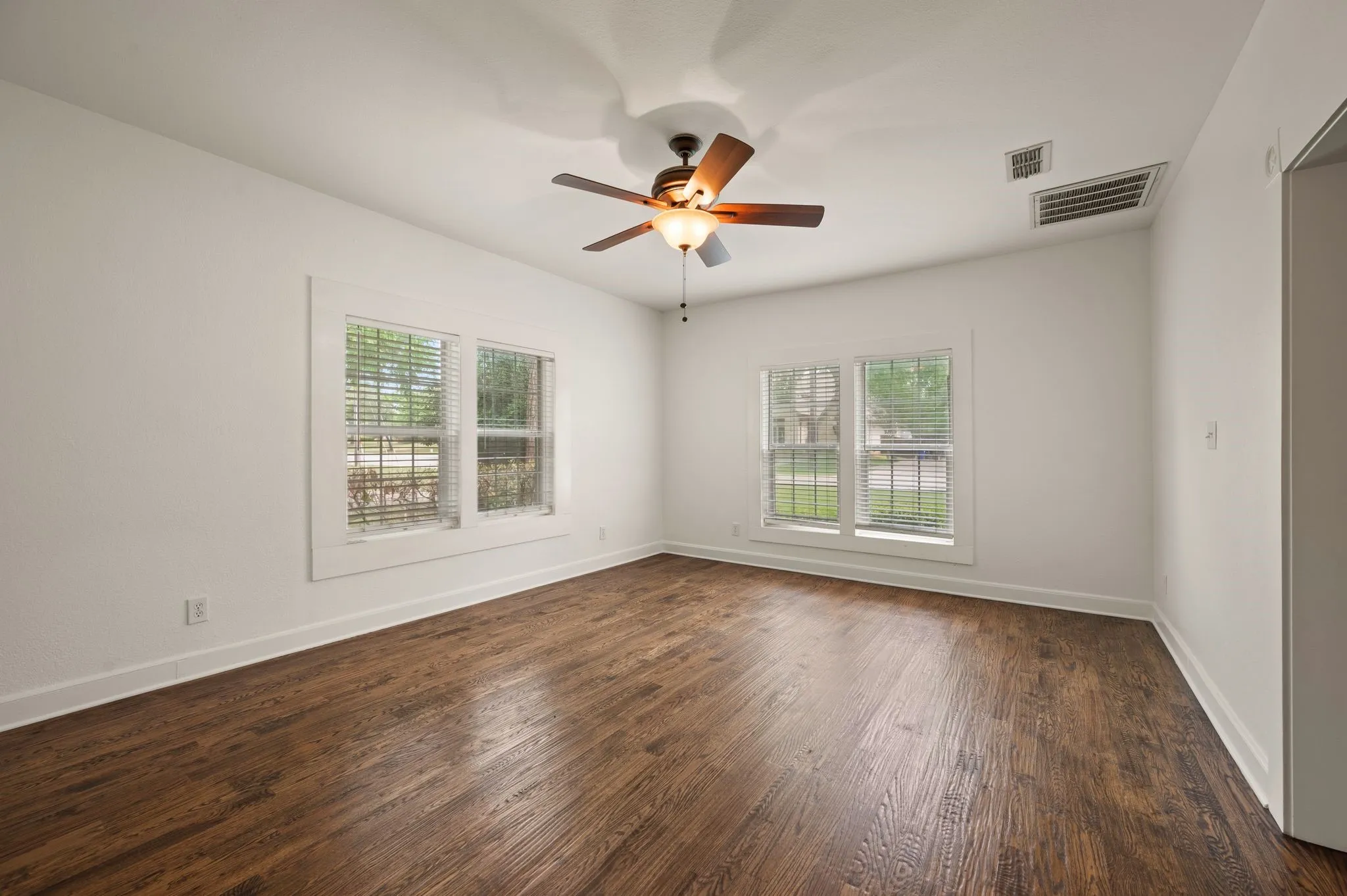 Unfurnished room featuring dark wood finished floors, visible vents, a ceiling fan, and a wealth of natural light