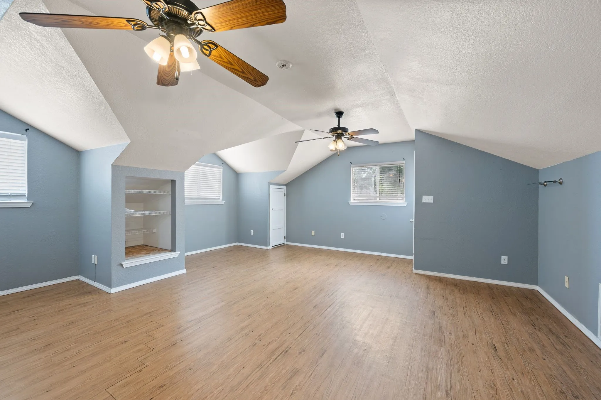 Bonus room featuring wood finished floors, a textured ceiling, a ceiling fan, and plenty of natural light