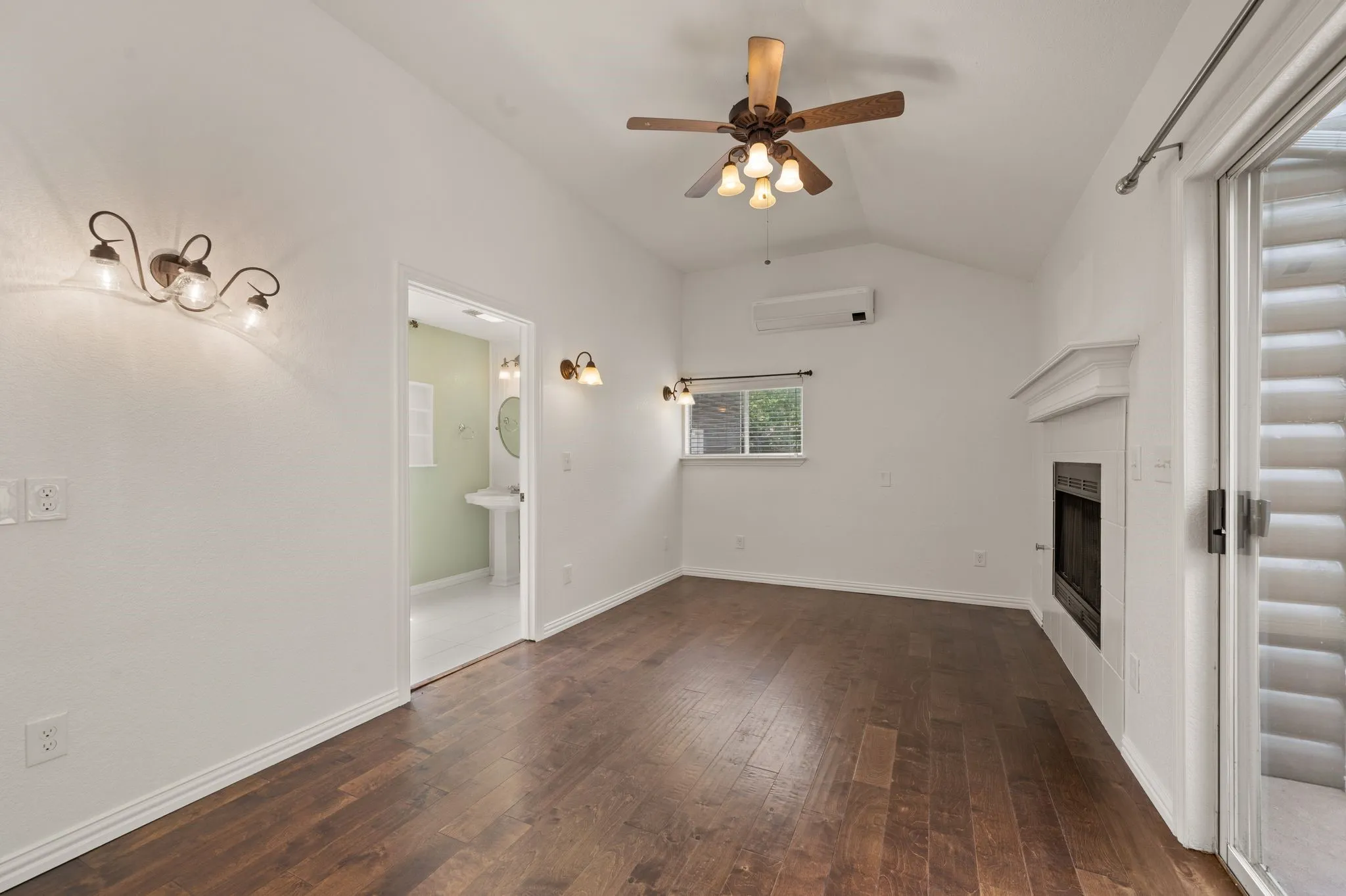 Unfurnished living room with vaulted ceiling, a ceiling fan, a glass covered fireplace, a wall mounted AC, and dark wood-type flooring