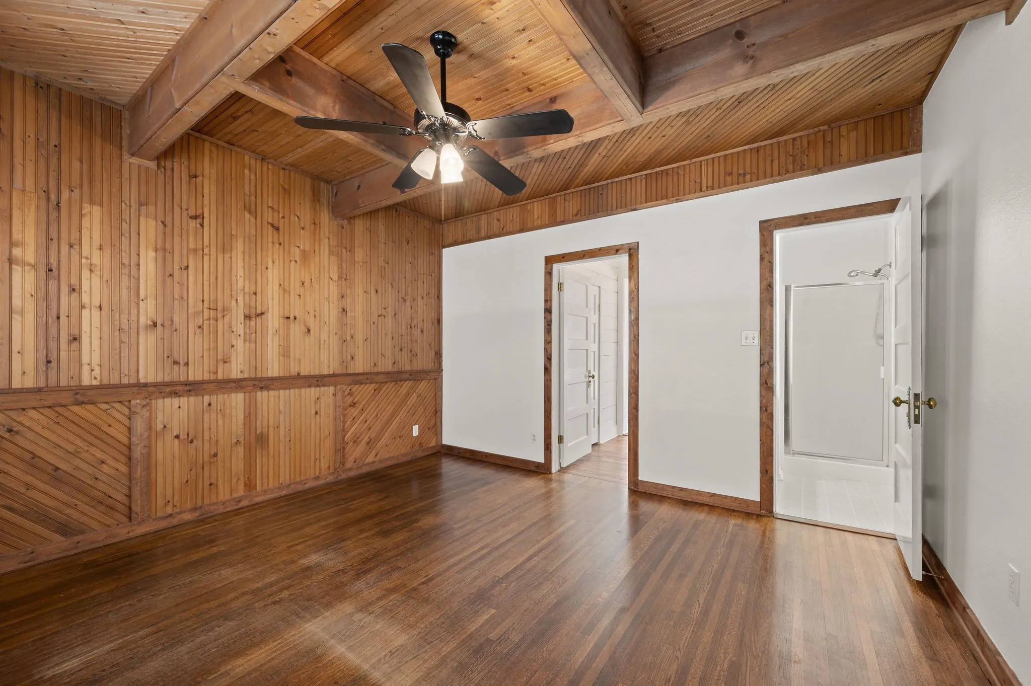 Unfurnished room featuring wooden walls, wooden ceiling, beamed ceiling, dark wood finished floors, and baseboards