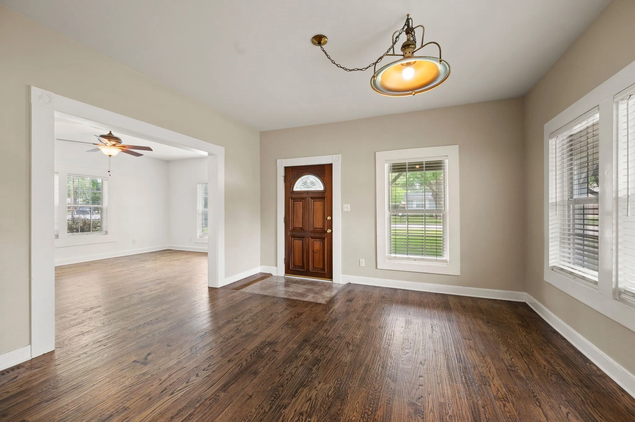 Entrance foyer featuring ceiling fan with notable chandelier, plenty of natural light, baseboards, and dark wood-type flooring