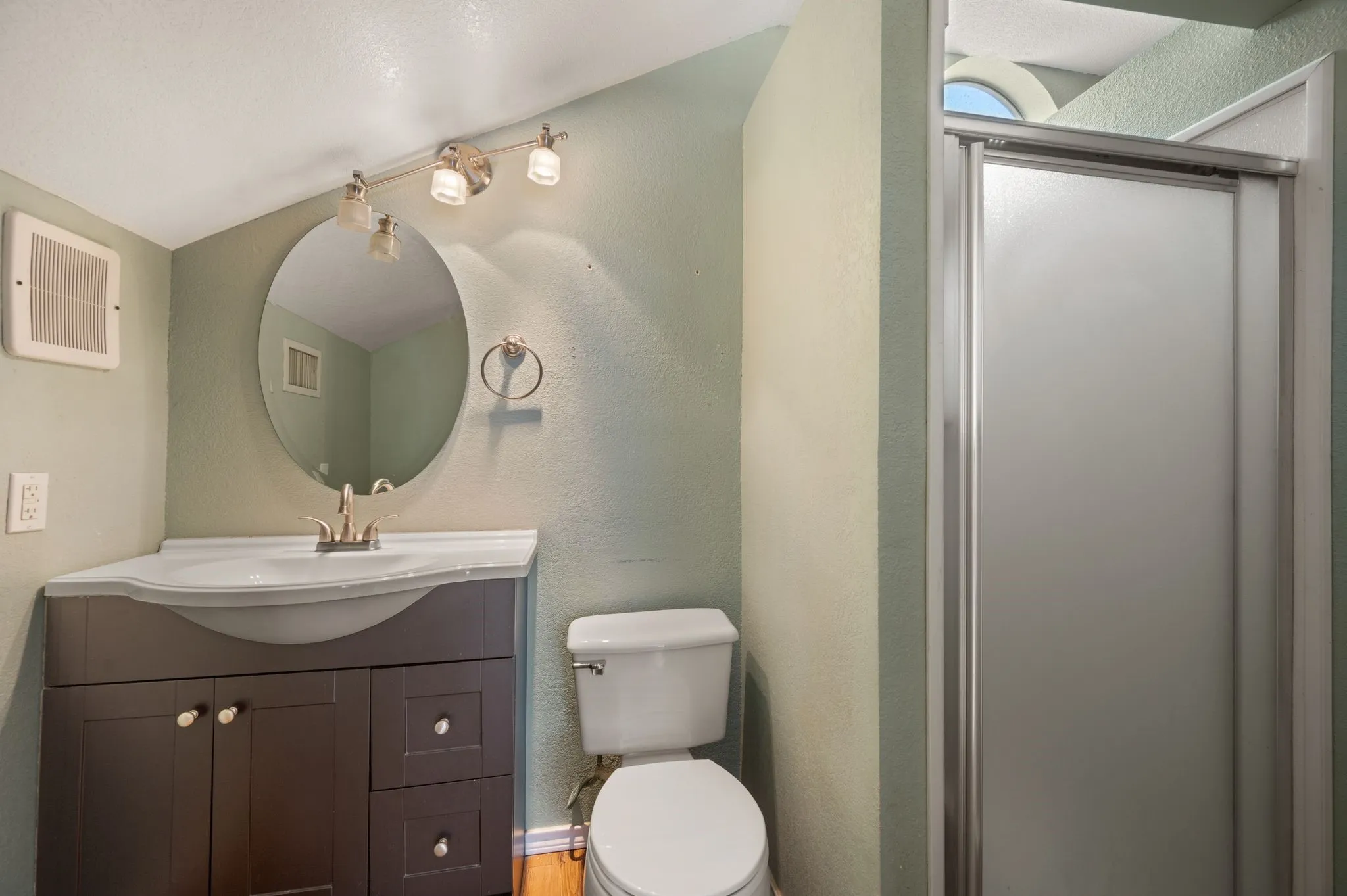 Full bathroom with toilet, visible vents, a shower stall, a textured wall, and vanity