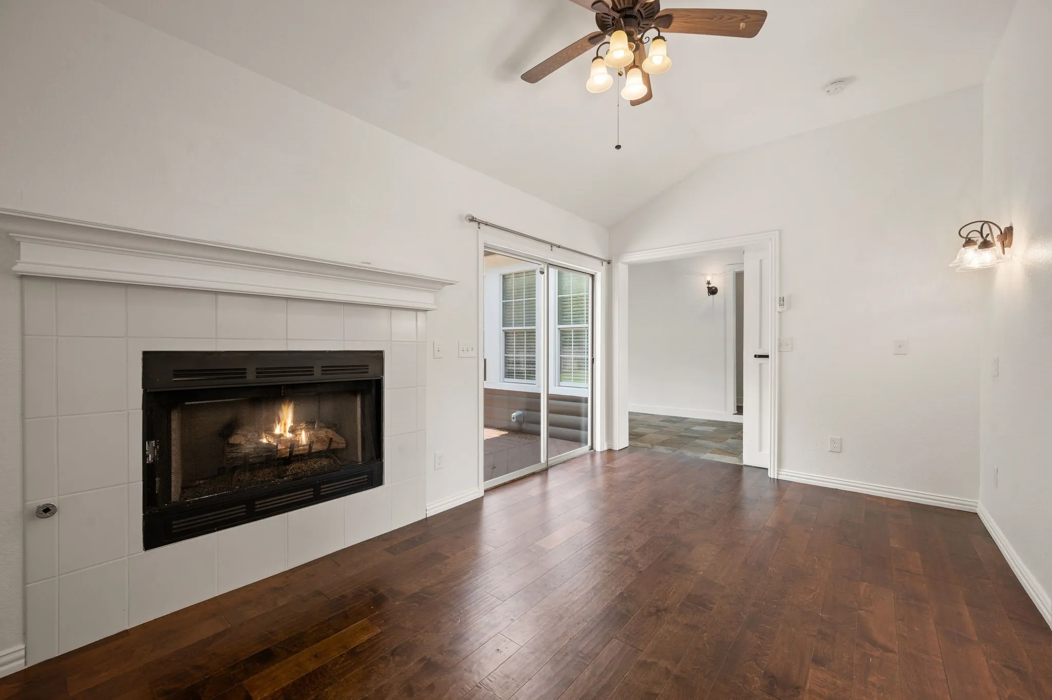 Unfurnished living room with ceiling fan, vaulted ceiling, wood finished floors, and a fireplace