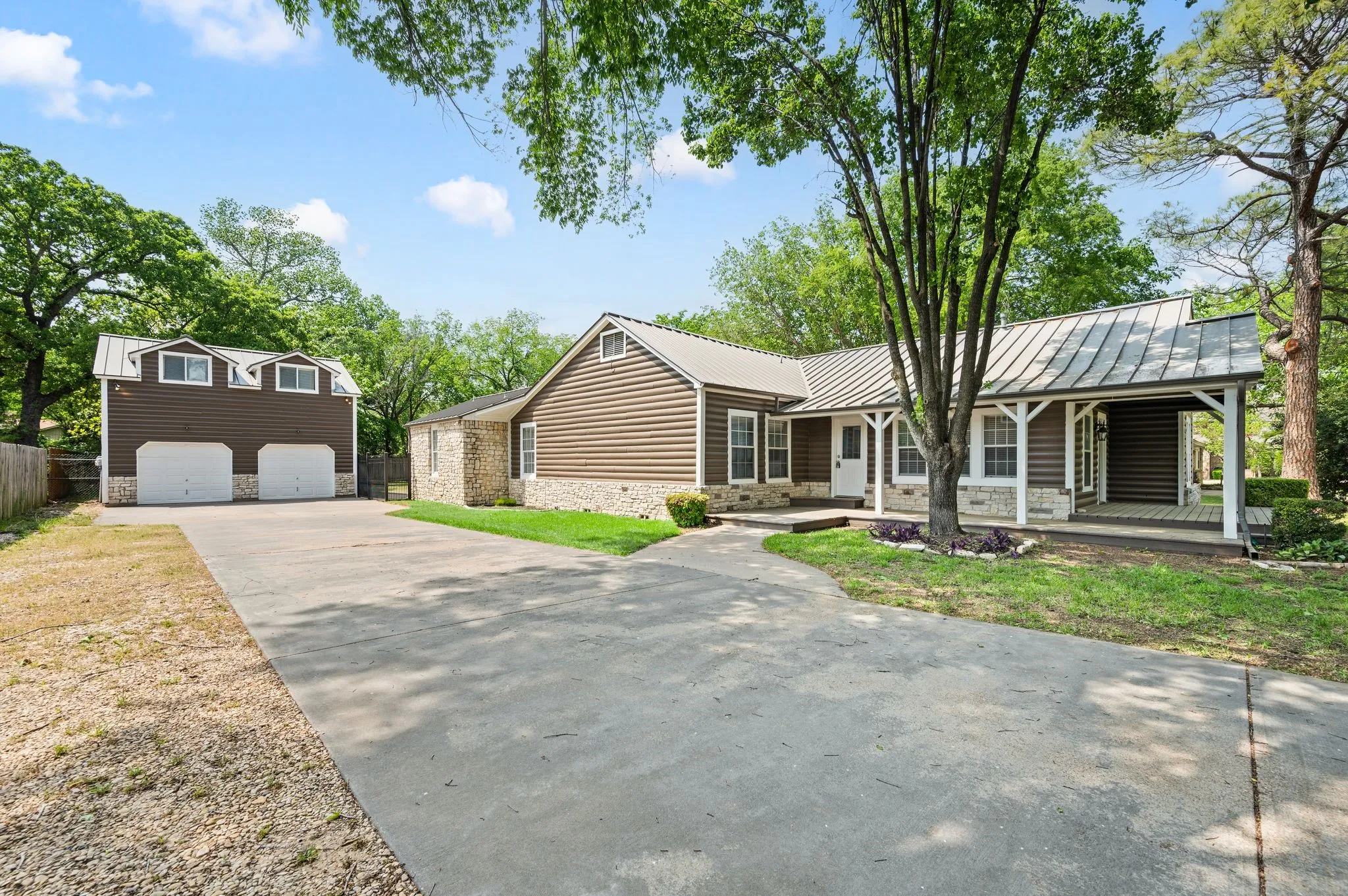 View of front of property with driveway, stone siding, a porch, metal roof, and a standing seam roof