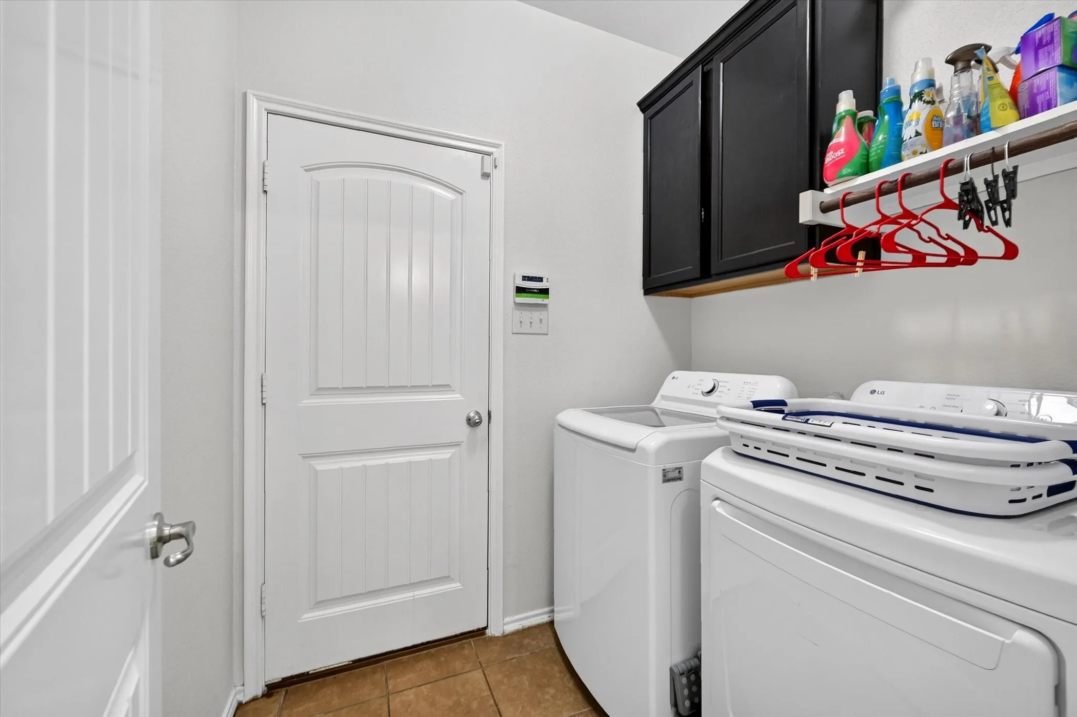 Laundry area with tiled flooring, white walls, dark cabinetry, and an open shelving unit