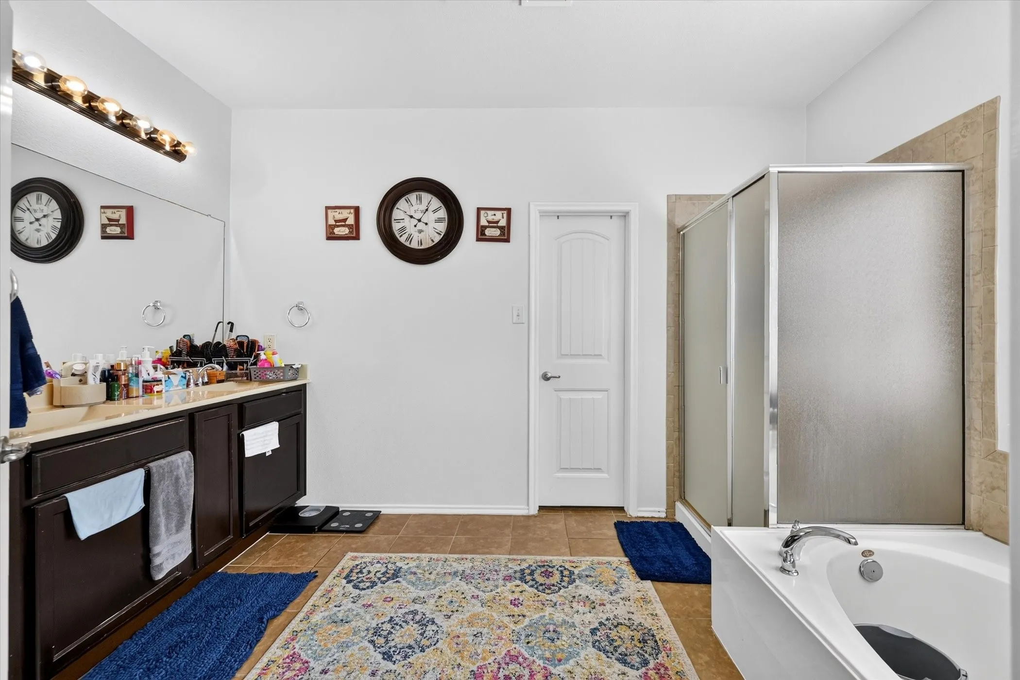 Vanity with dark wood-finish cabinetry, built-in soaking tub, separate shower with frosted glass enclosure, and tile flooring