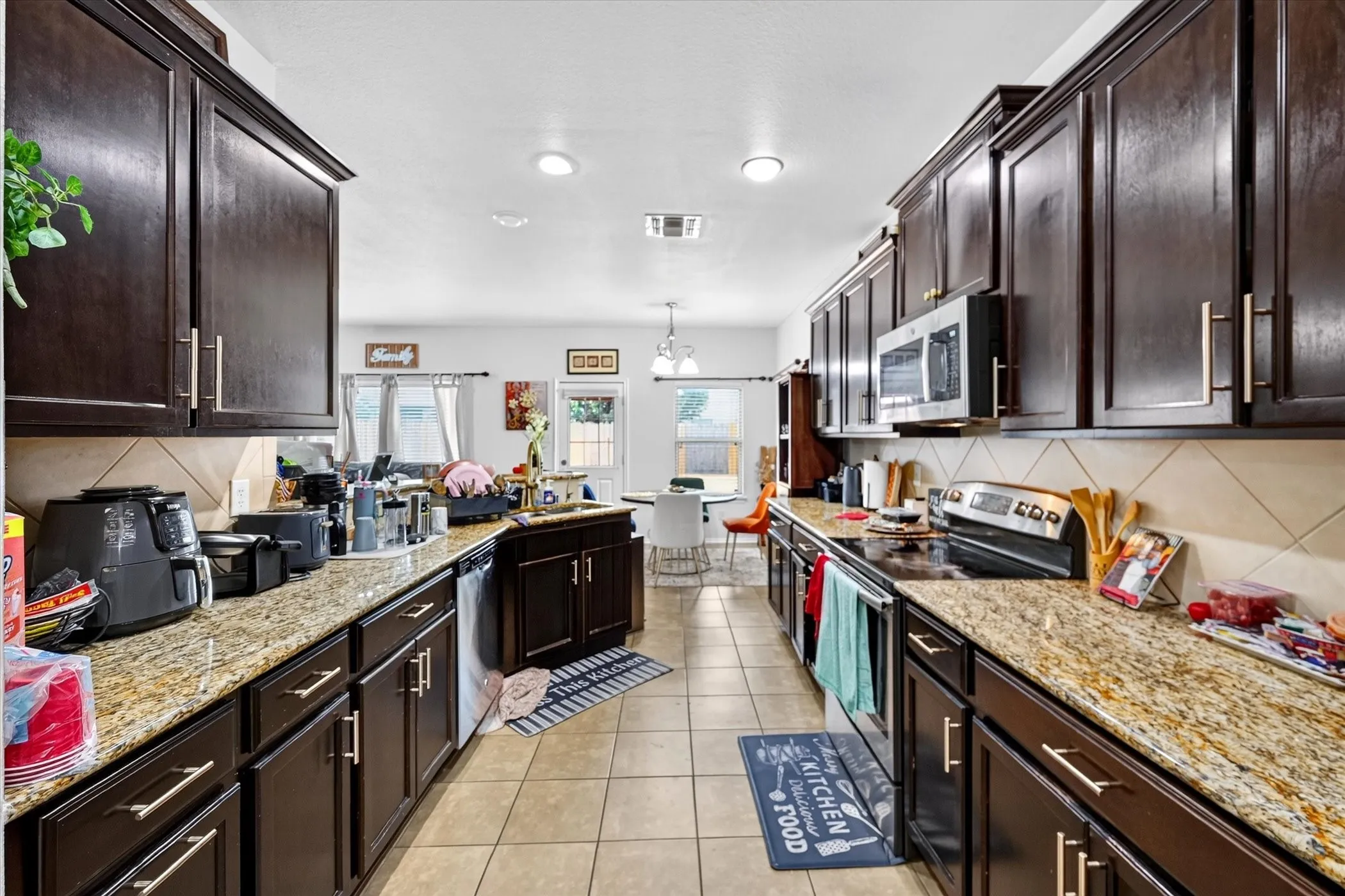 Galley kitchen featuring dark wood cabinetry, light-toned granite countertops, and tile flooring