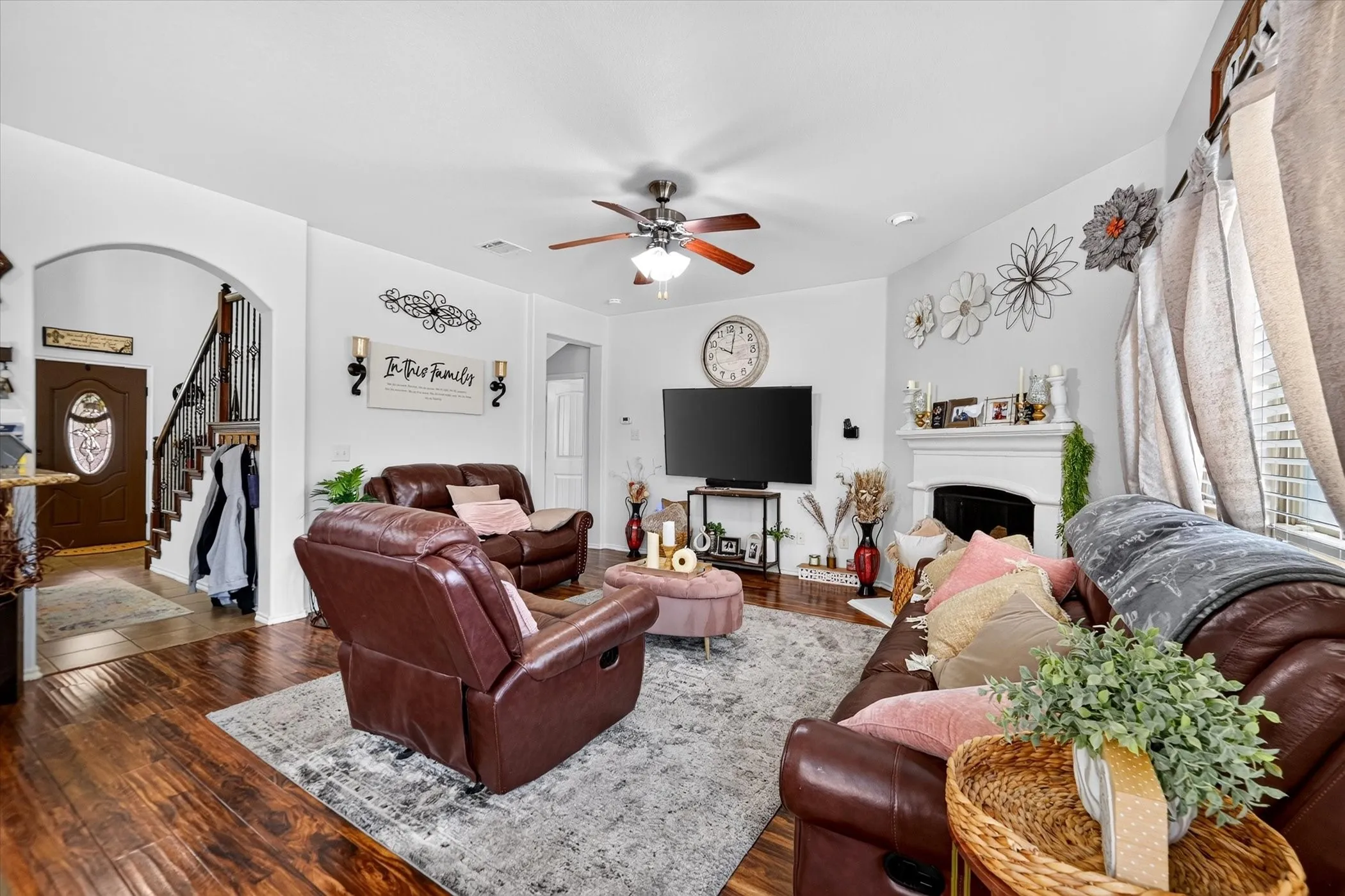 Vaulted ceiling, wood-finish flooring, white painted fireplace, ceiling fan with integrated lighting, and an arched entry
