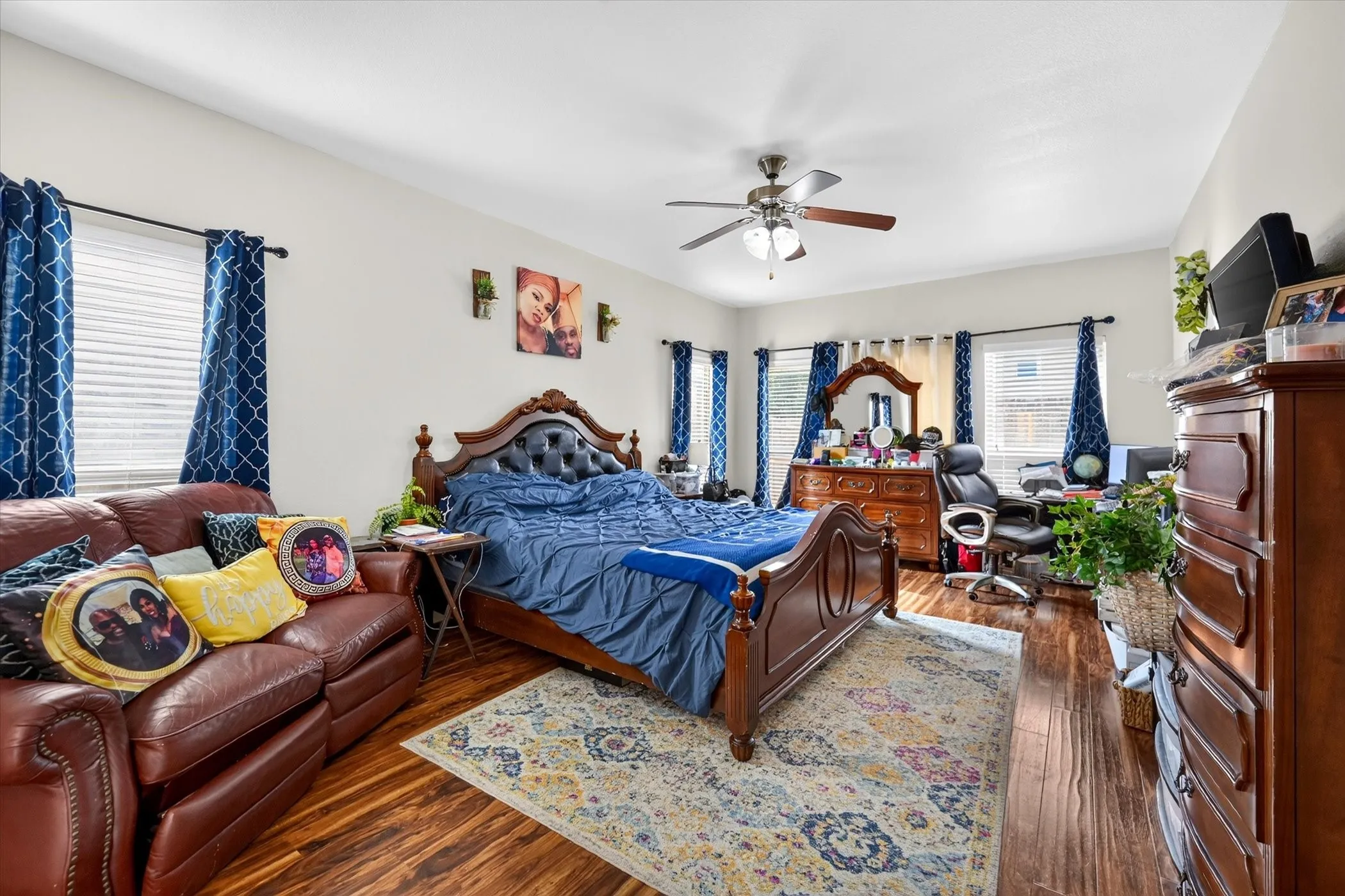 Hardwood-look flooring, multiple windows with blinds, ceiling fan with integrated lighting, and white wall finishes