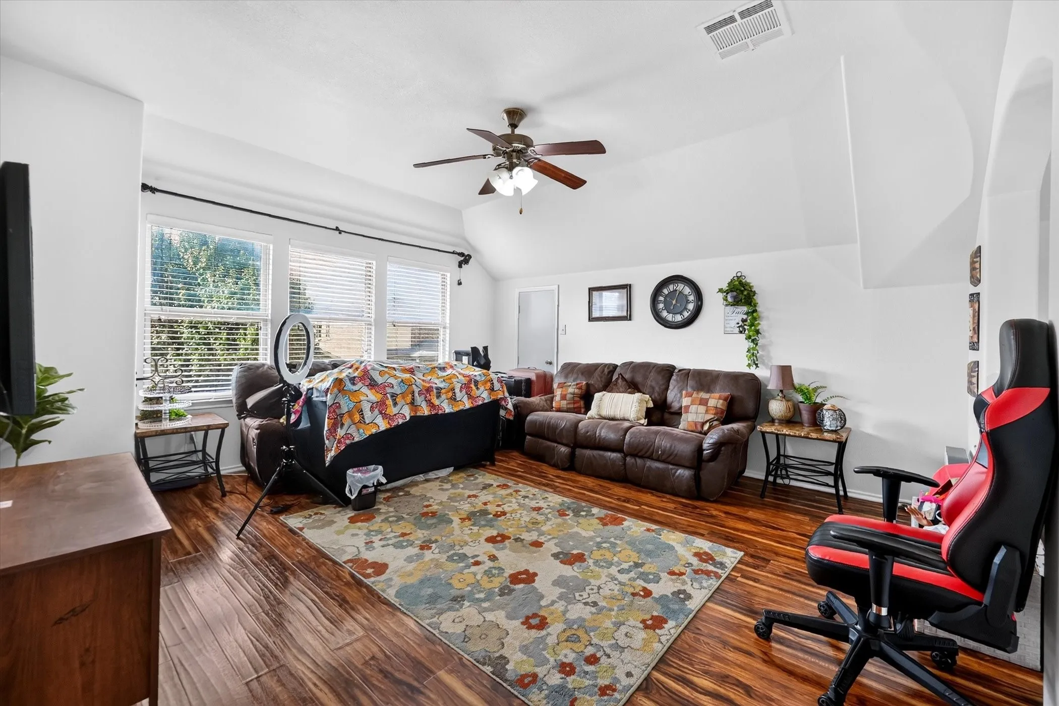 Vaulted ceiling, ceiling fan with integrated lighting, wood-finish flooring, white walls, multiple windows with blinds