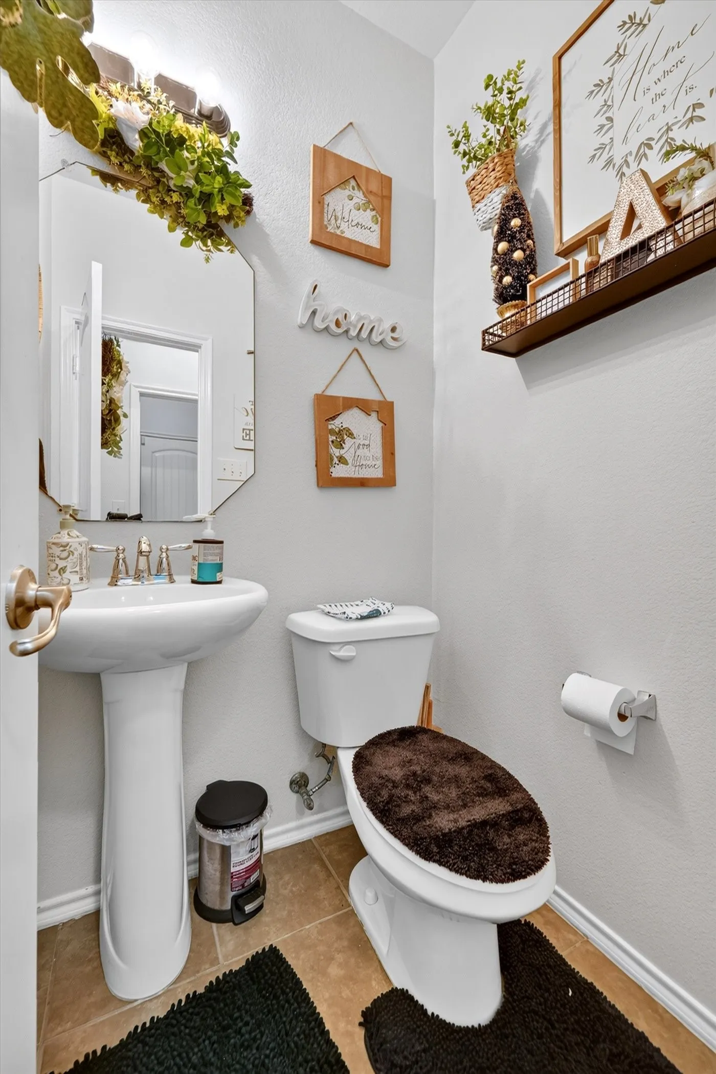 Pedestal sink with polished chrome fixtures, octagonal mirror, wall-mounted lighting, and tile flooring