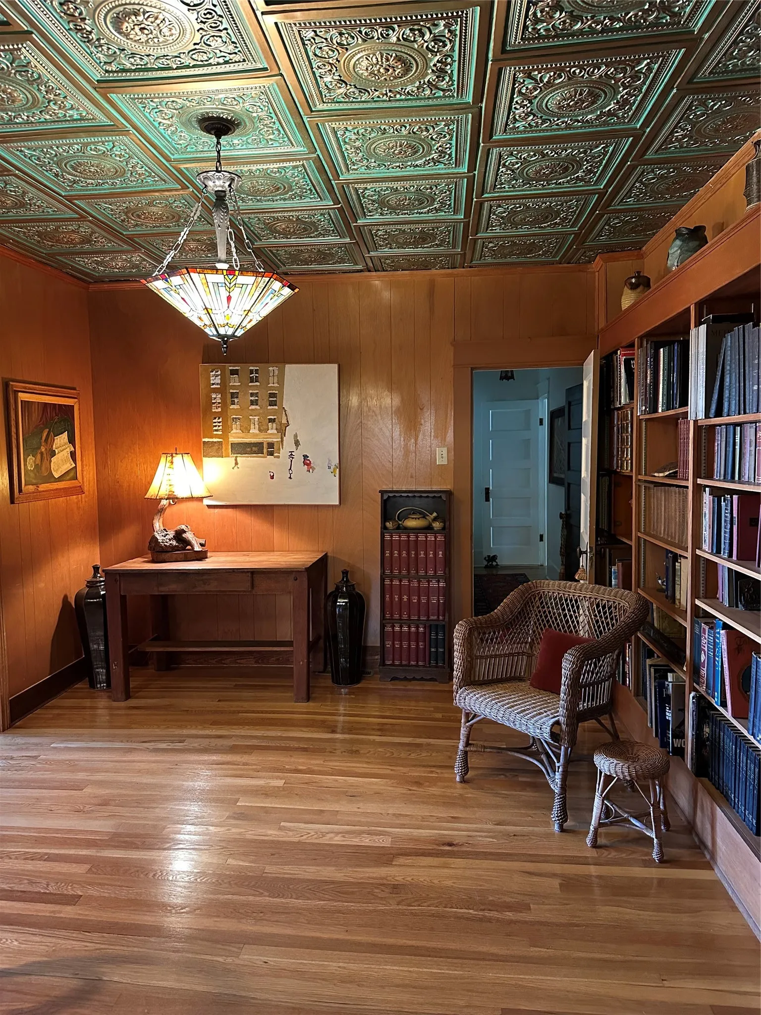 Ornate pressed tin ceiling, wood paneling, wood-finish flooring, built-in shelving, and a decorative pendant light fixture