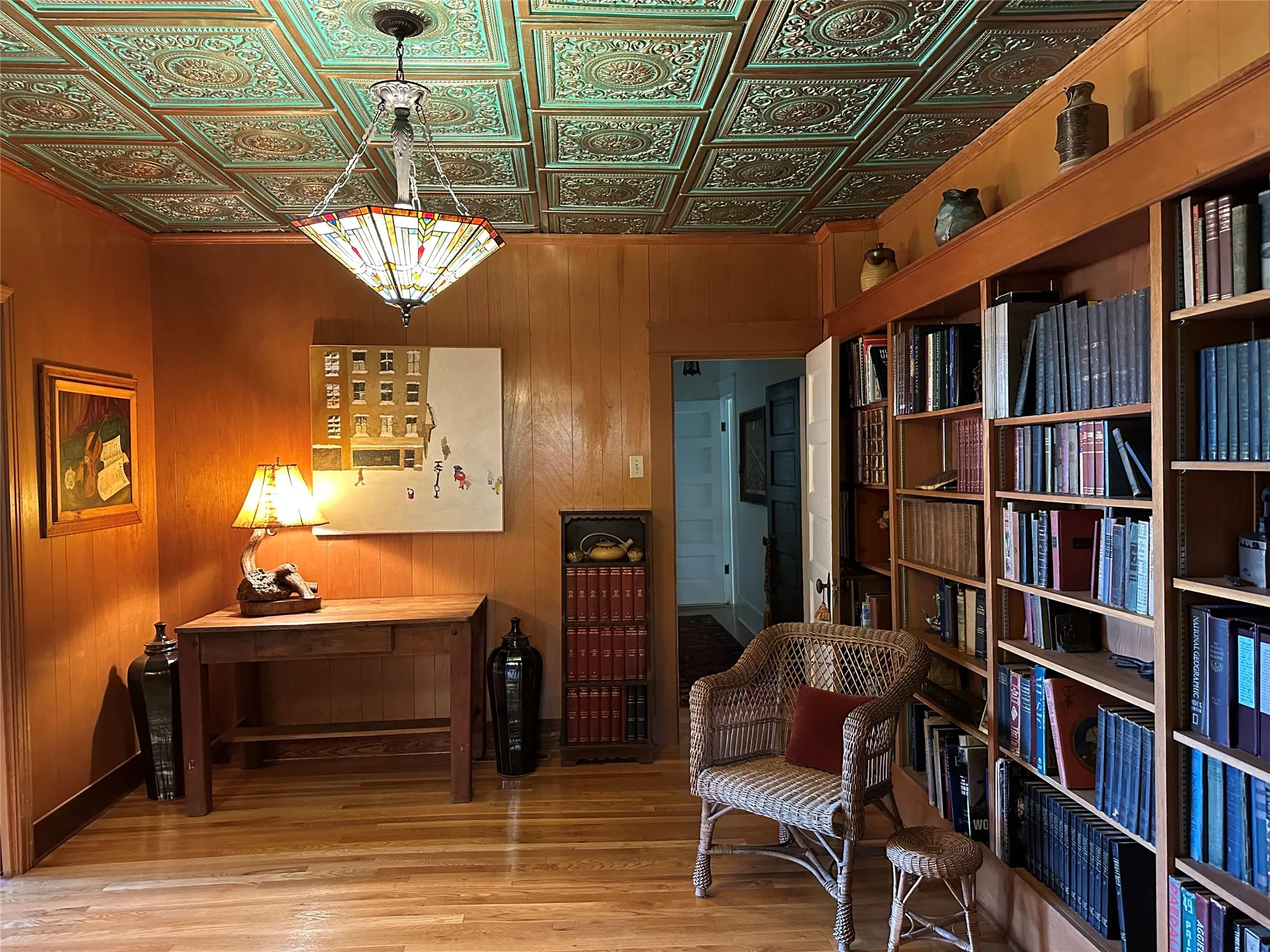 Ornate tin ceiling, wood-finish flooring, built-in shelving, wood wall paneling, and an interior doorway