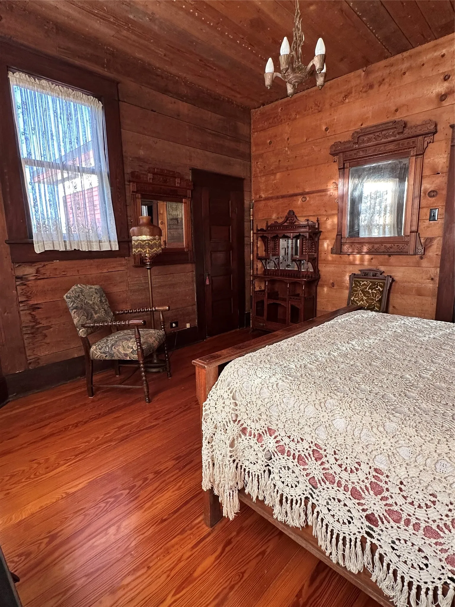 Hardwood flooring, wood-paneled walls, wood-paneled ceiling, wood-framed window, and a chandelier