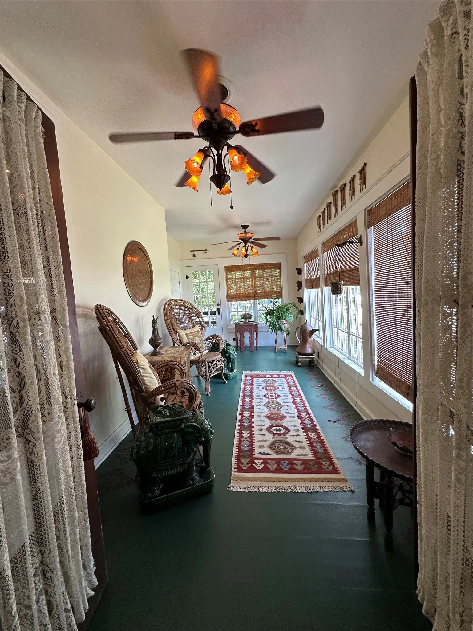 Sunroom with a painted floor, multiple windows, and two ceiling fans with integrated lighting