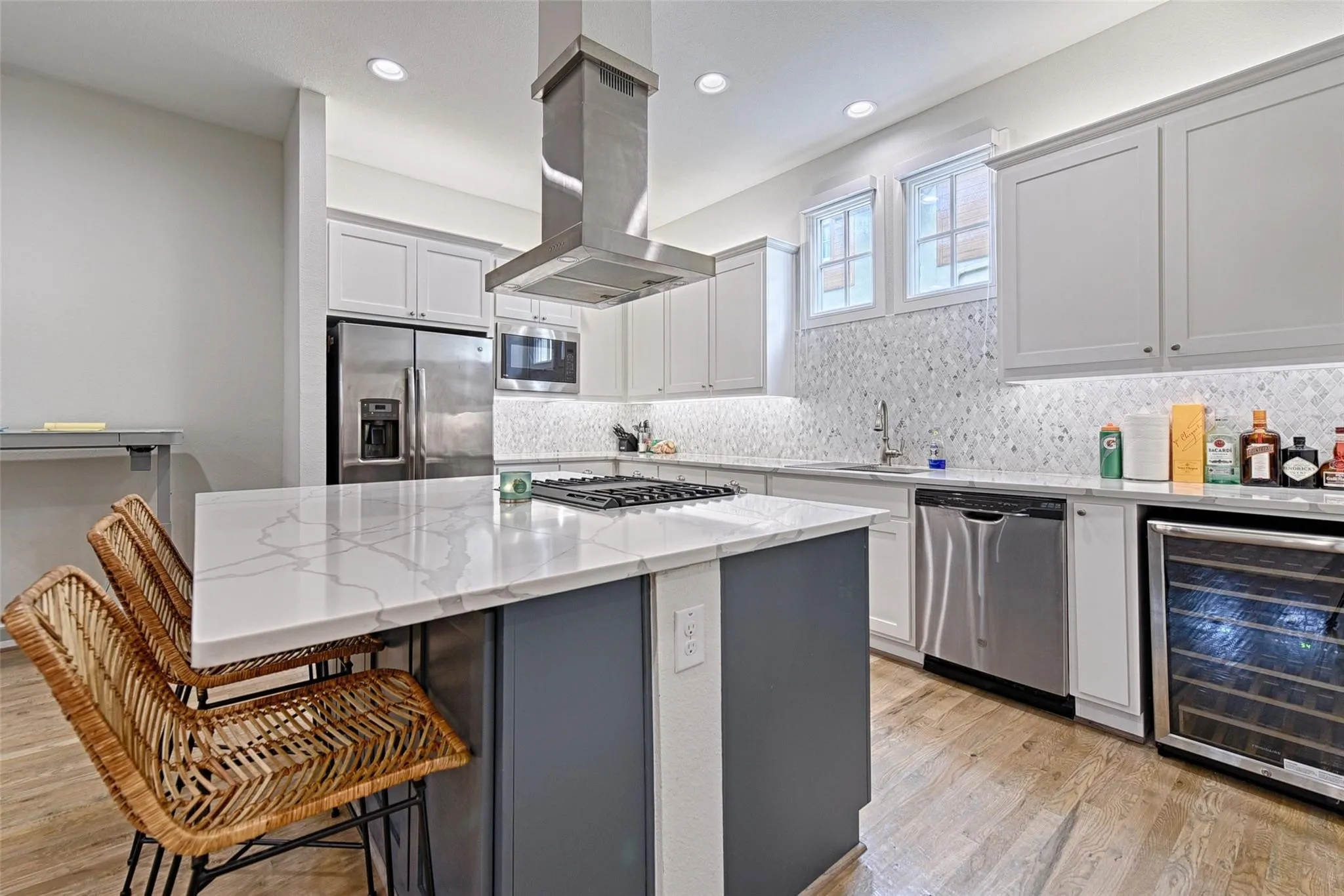 Modern kitchen featuring white shaker cabinetry, stainless steel appliances, a white quartz island with seating, a mosaic tile backsplash, and light wood-finish flooring