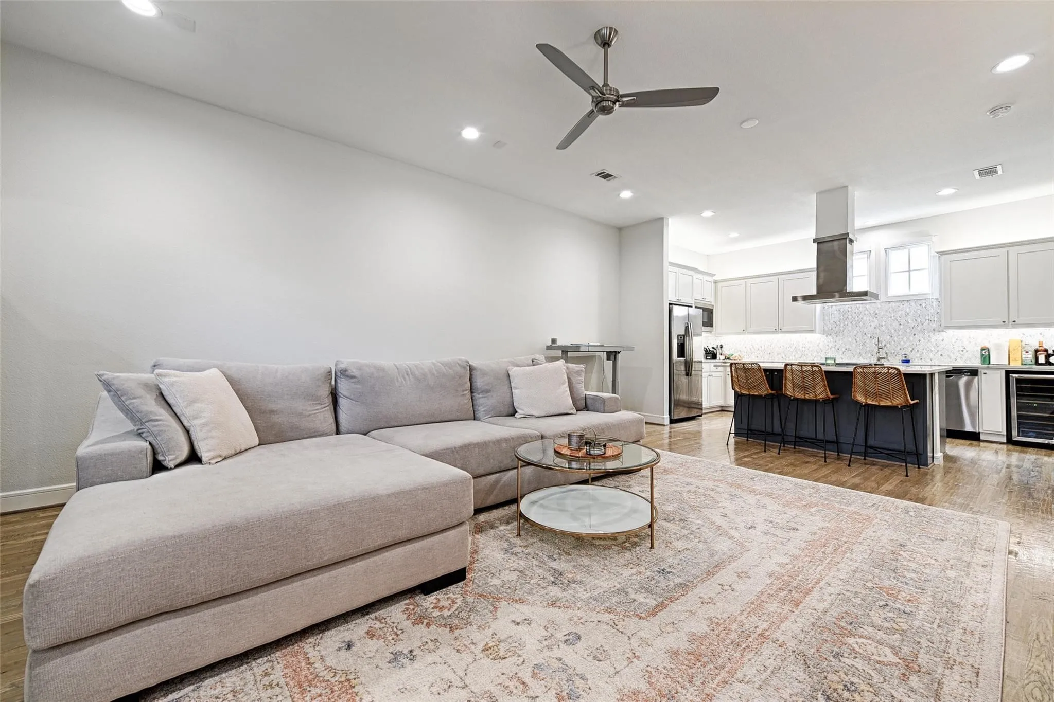 Recessed lighting, wood-finish flooring, kitchen island with seating, stainless steel appliances, and a built-in beverage cooler