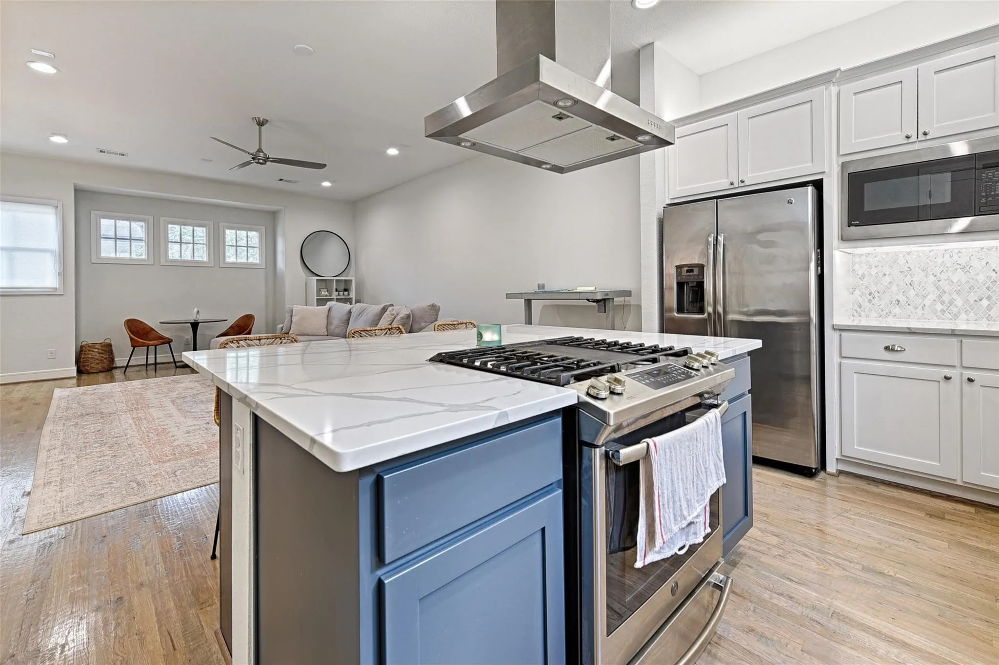 Kitchen island with a light-toned countertop, stainless steel appliances, white cabinetry, and wood-finish flooring