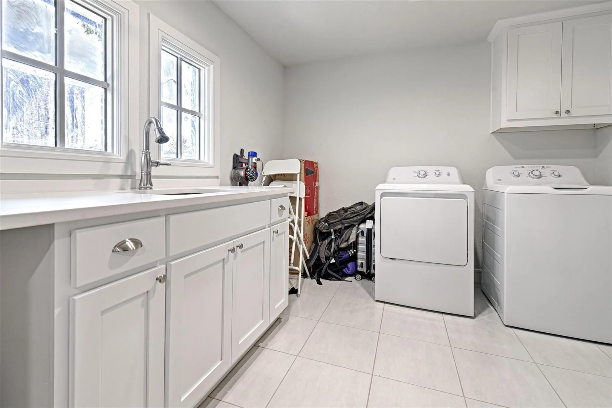 White shaker-style cabinetry with chrome hardware, an integrated sink with a pull-down faucet, and a light-toned countertop