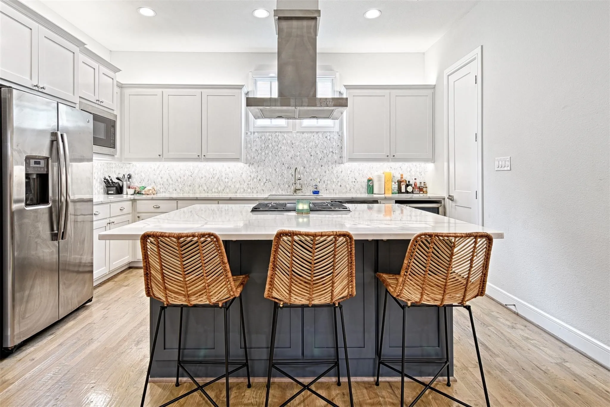 Kitchen featuring stainless steel appliances, white cabinetry, a large center island with seating, a gas cooktop, and wood-finish flooring