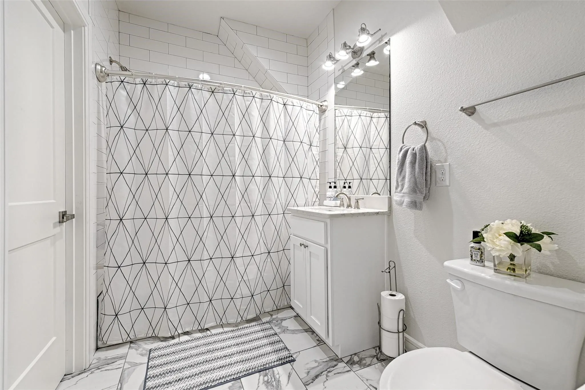 White subway tile shower surround, white vanity with integrated sink, chrome faucet, wall-mounted mirror, and white toilet
