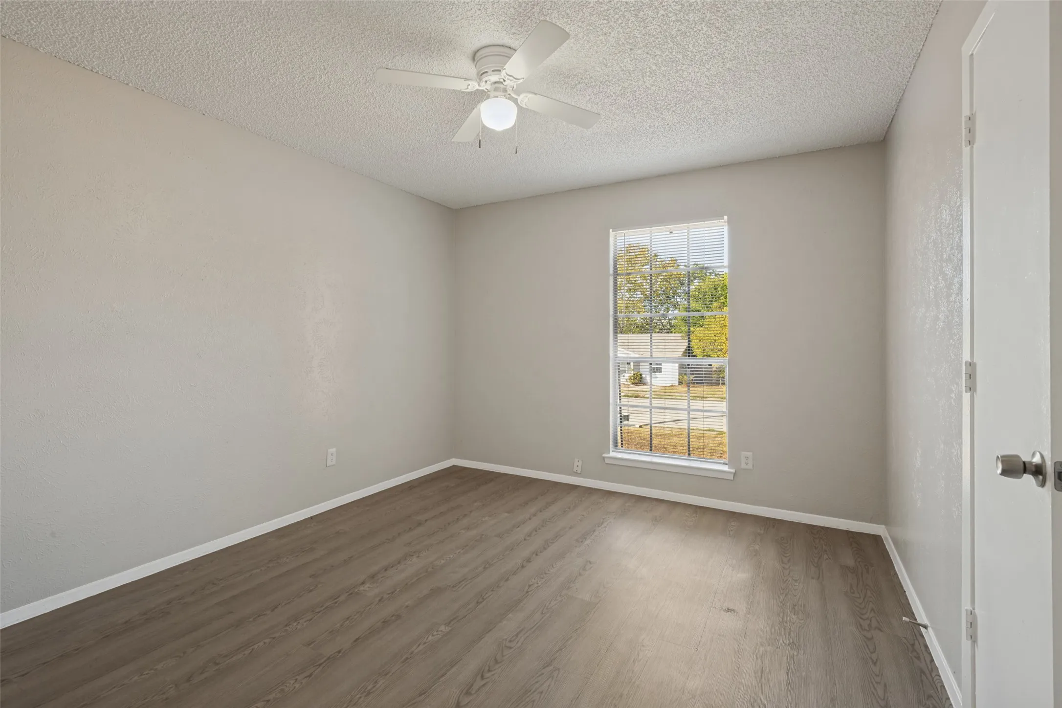 Wood-finish flooring with white trim, a single window, and a ceiling fan with light fixture