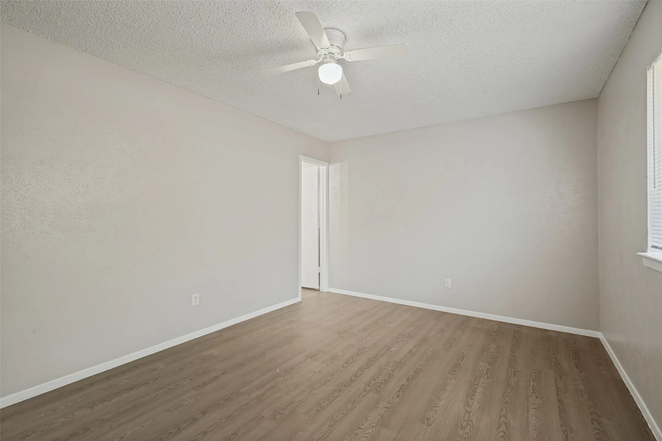 Wood-finish flooring, neutral wall tones, ceiling fan with integrated lighting, and window with blinds