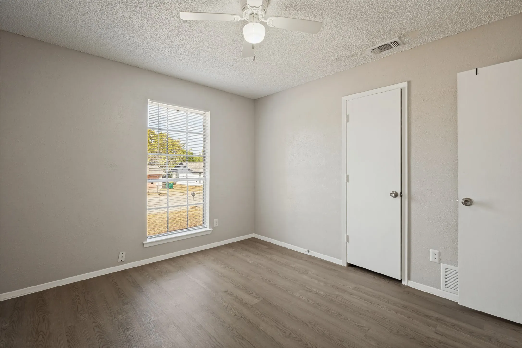 Wood-finish flooring, white trim, ceiling fan, and window with horizontal blinds
