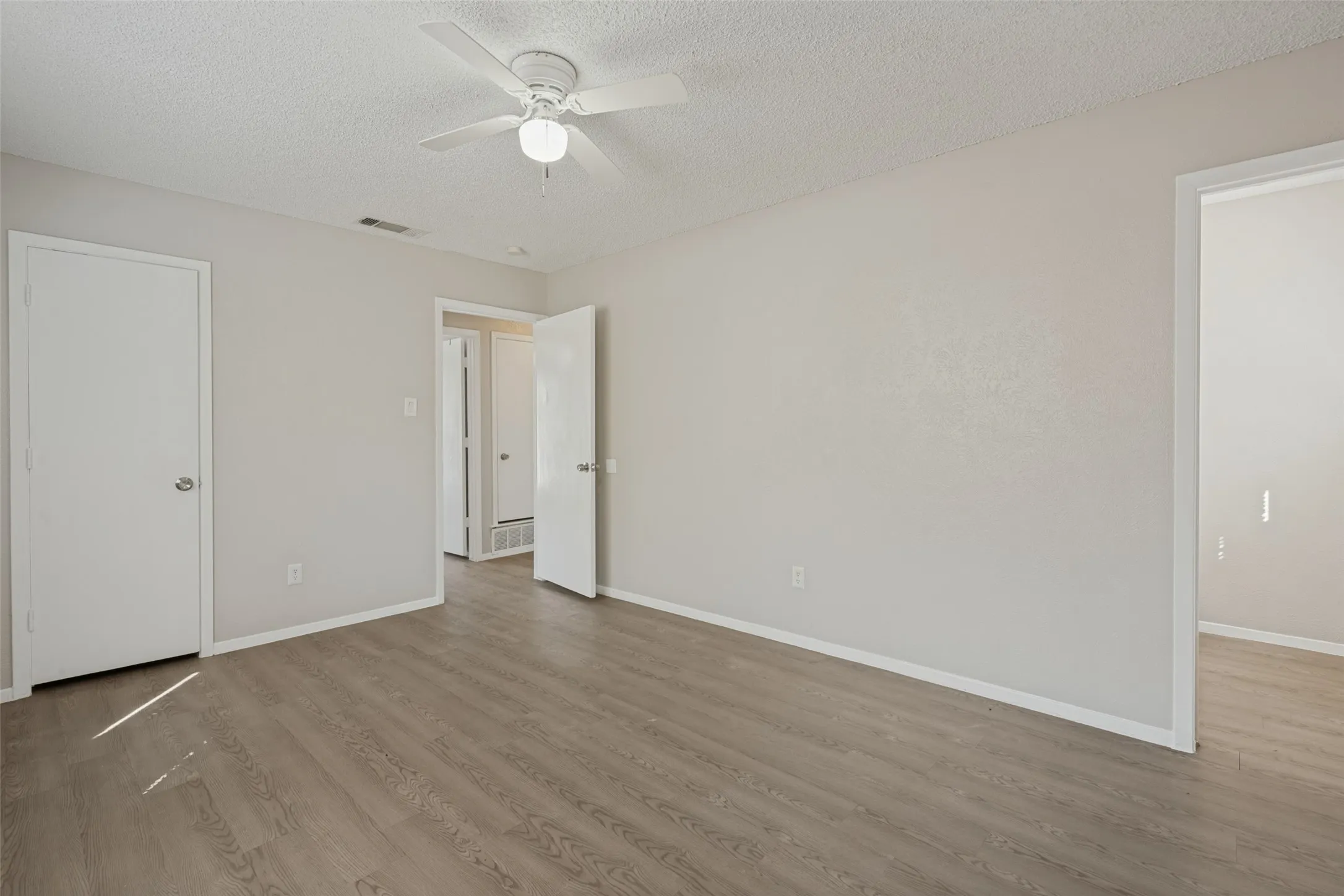 Room featuring wood-finish flooring, light neutral wall paint, and a ceiling fan with integrated lighting